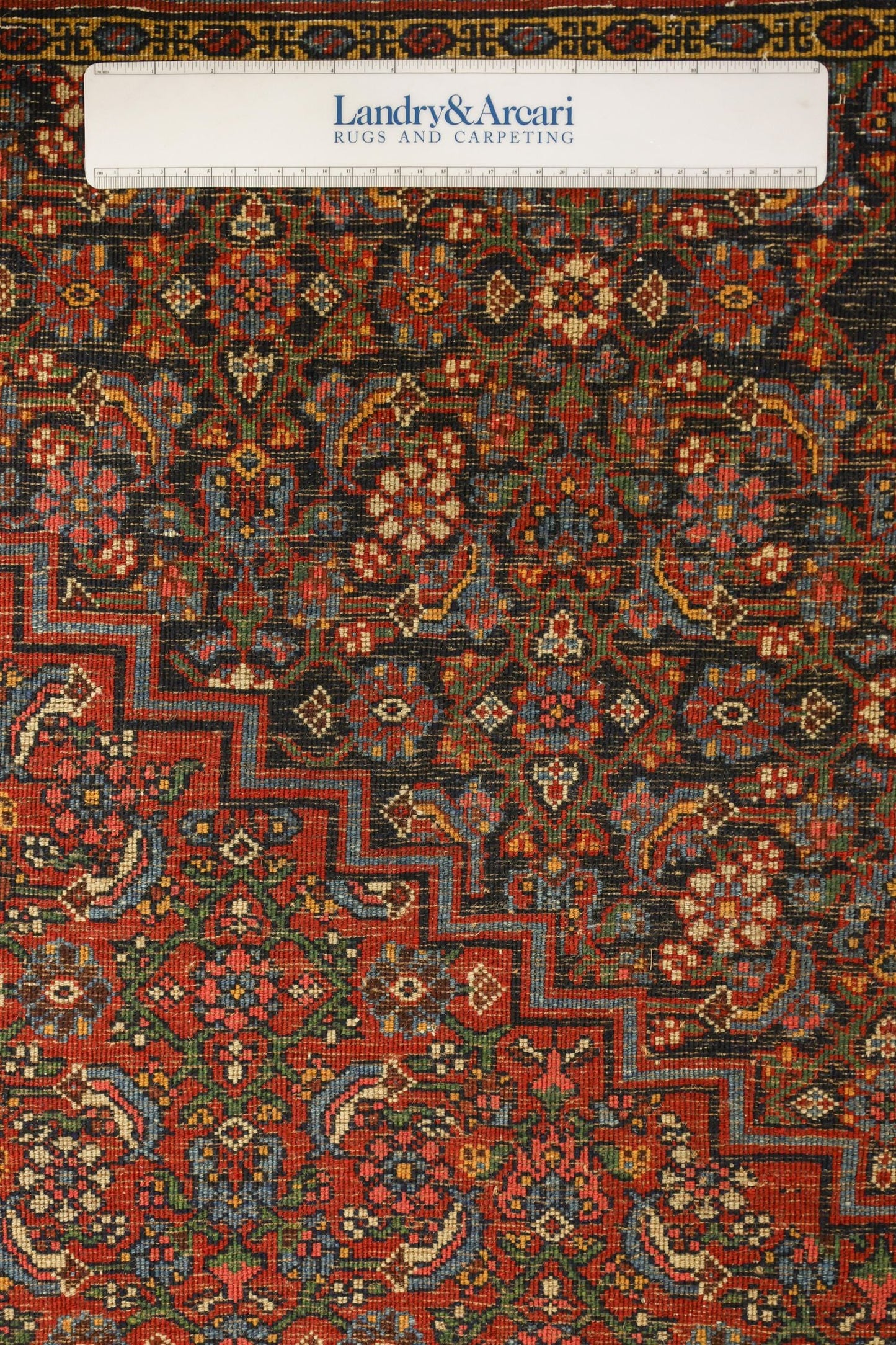 Detailed close-up of an antique Bijar rug's intricate, handwoven floral pattern in rich reds, blues, and greens.