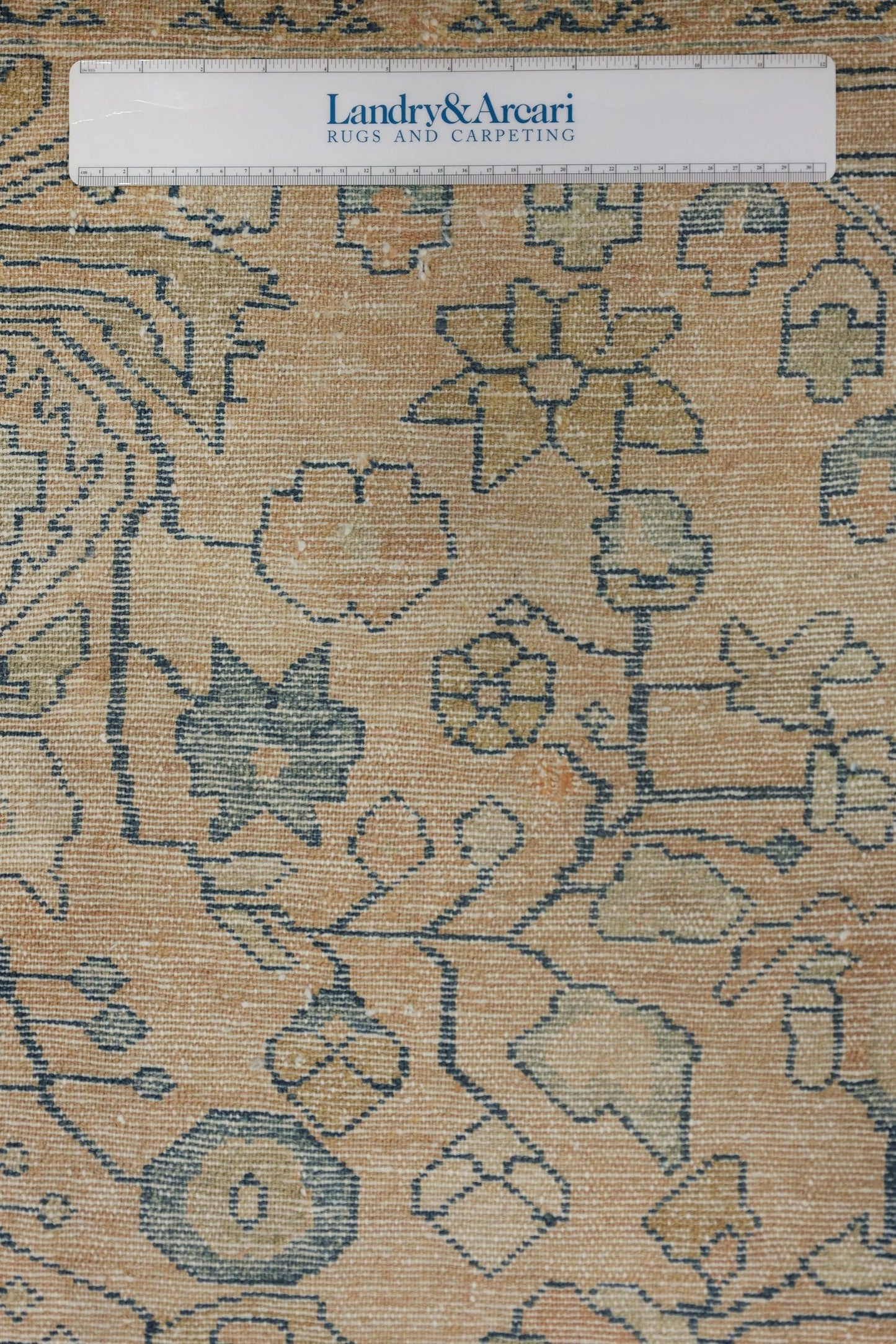 Close-up detail of a handwoven rug with a beige background and a muted blue floral pattern.