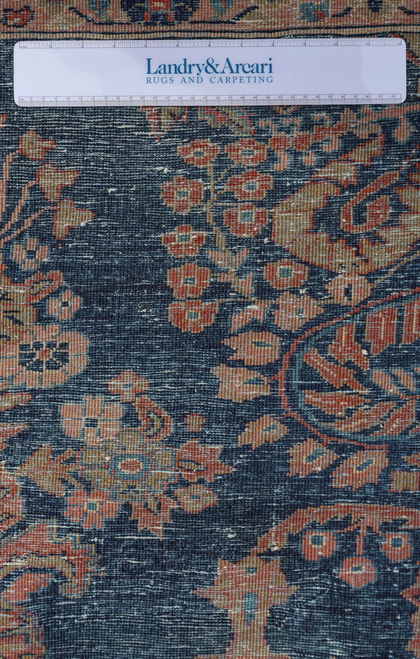 Detailed close-up of a traditional handwoven rug with a deep blue background and intricate red and beige floral patterns.