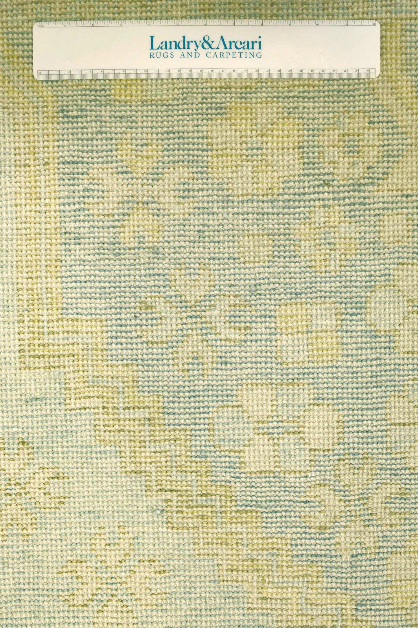 Close-up of handwoven rug displaying a muted green and beige pattern.