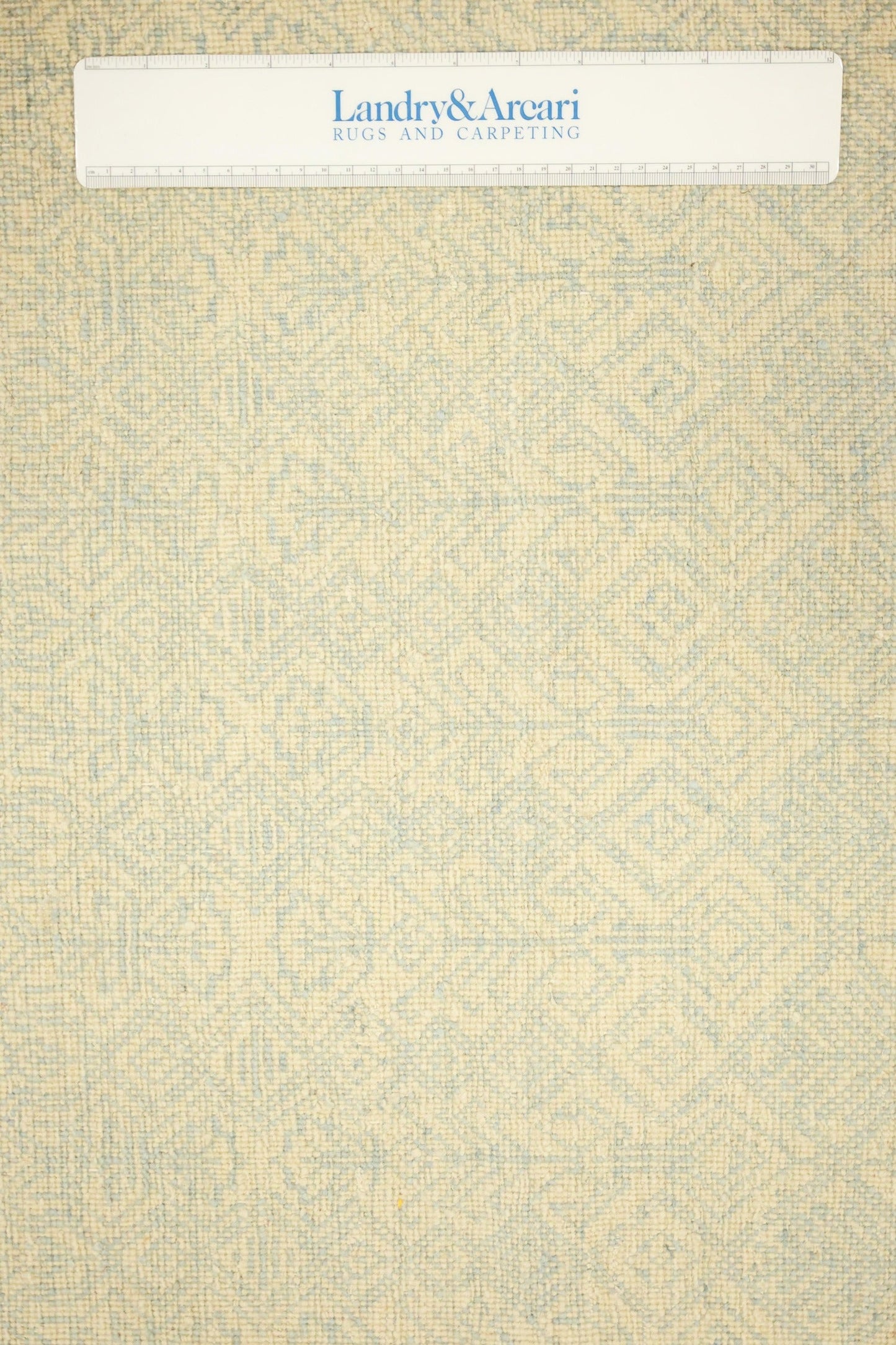 Close-up of handwoven rug texture, creamy beige with subtle light blue pattern.