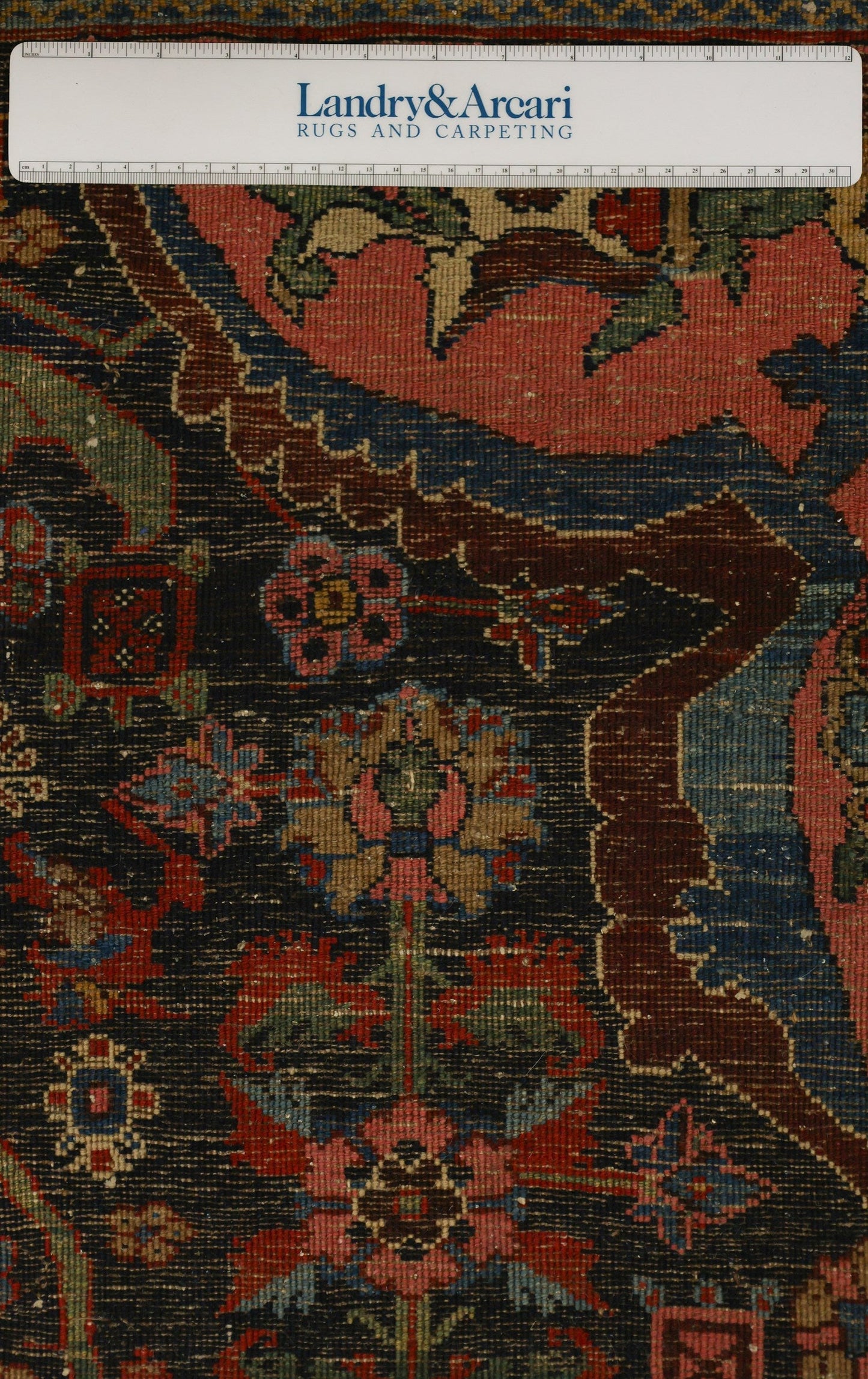 Close-up detail of an antique Bijar rug's intricate, handwoven floral pattern in rich reds, blues, and greens on a dark background.