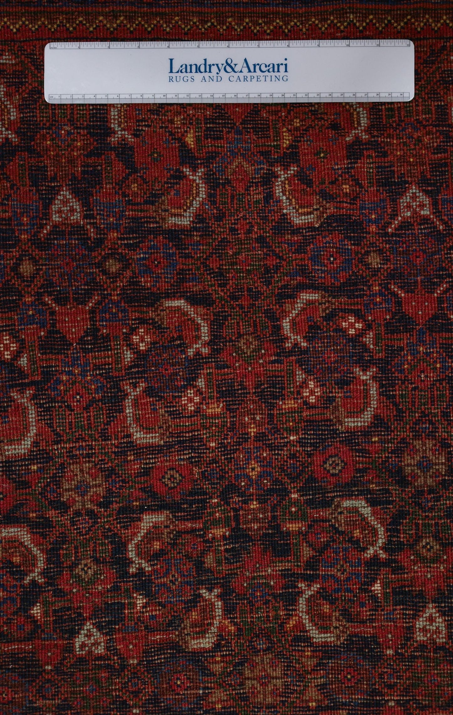 Close-up detail of a handwoven rug, showcasing intricate red and navy floral pattern.