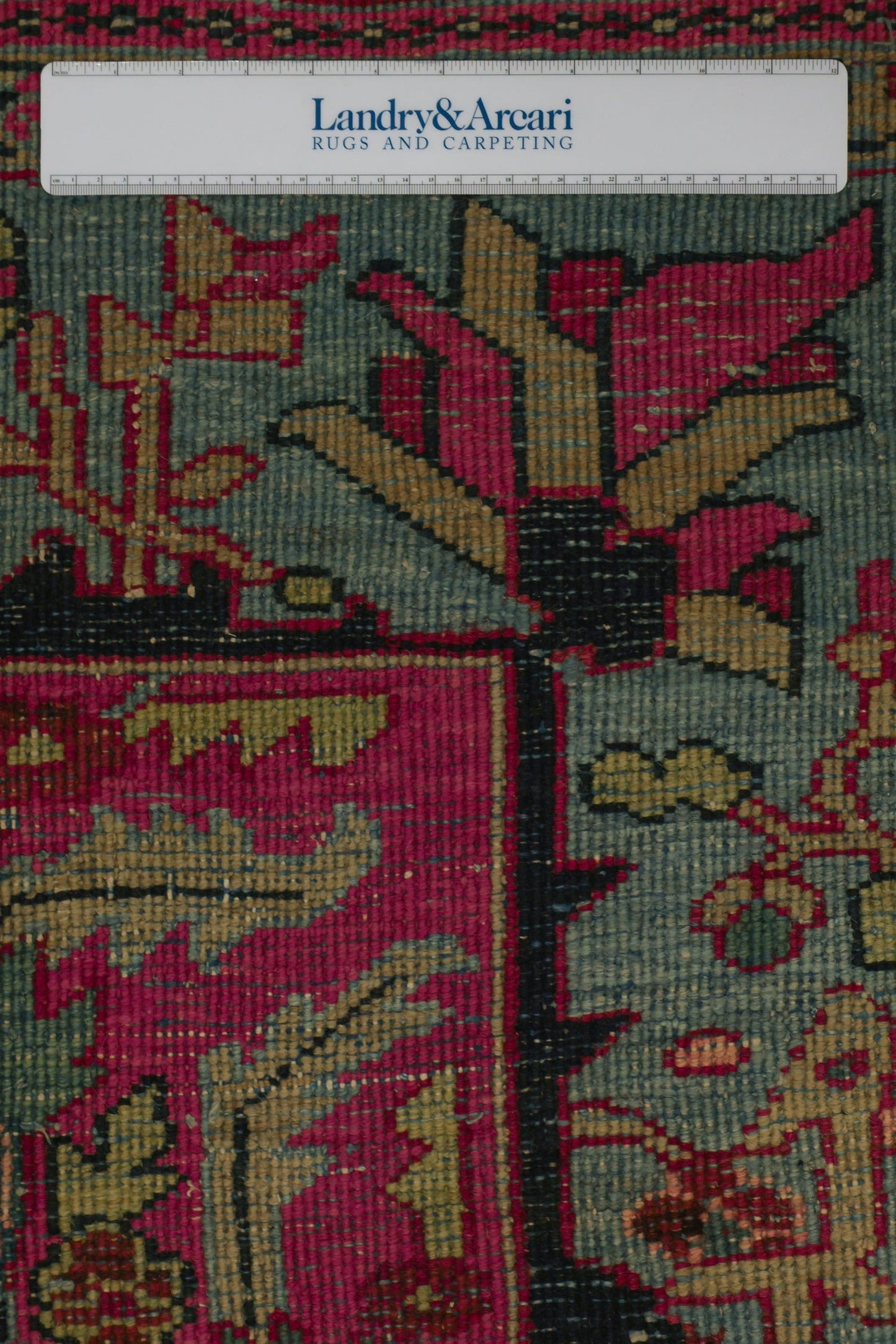 Close-up detail of antique Heriz rug's handwoven floral pattern in teal, pink, and gold.