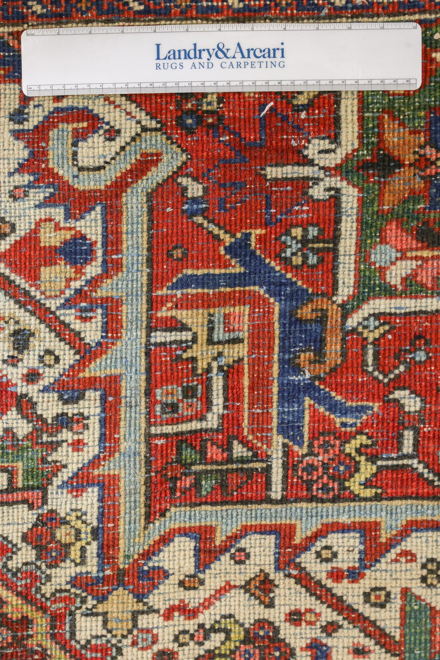 Close-up detail of antique Heriz rug's intricate handwoven pattern, showcasing vibrant reds, blues, and creams.