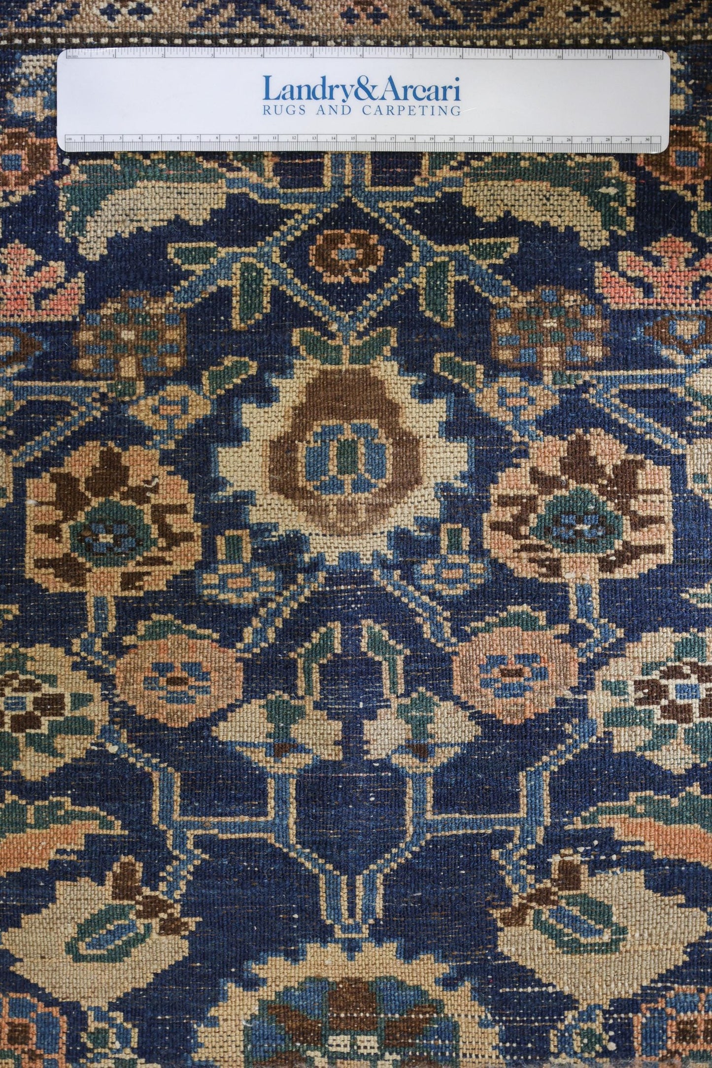 Close-up detail of antique Persian rug's handwoven floral pattern in navy, beige, and brown tones.