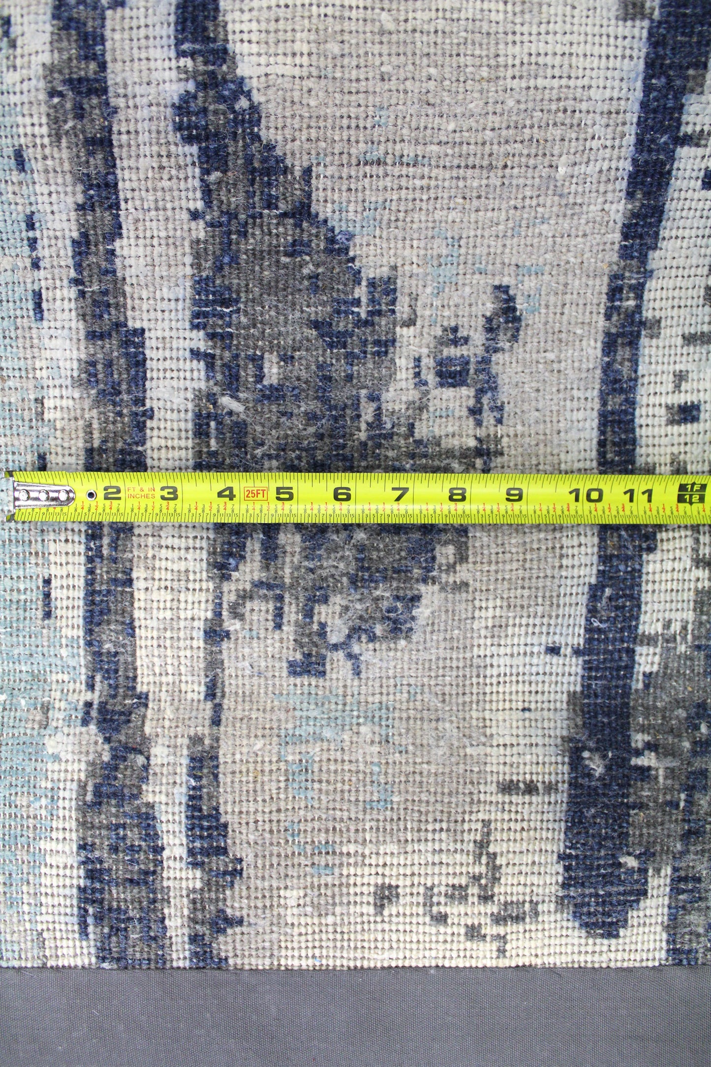 Close-up detail of handwoven rug in blues and grays, measured with tape.
