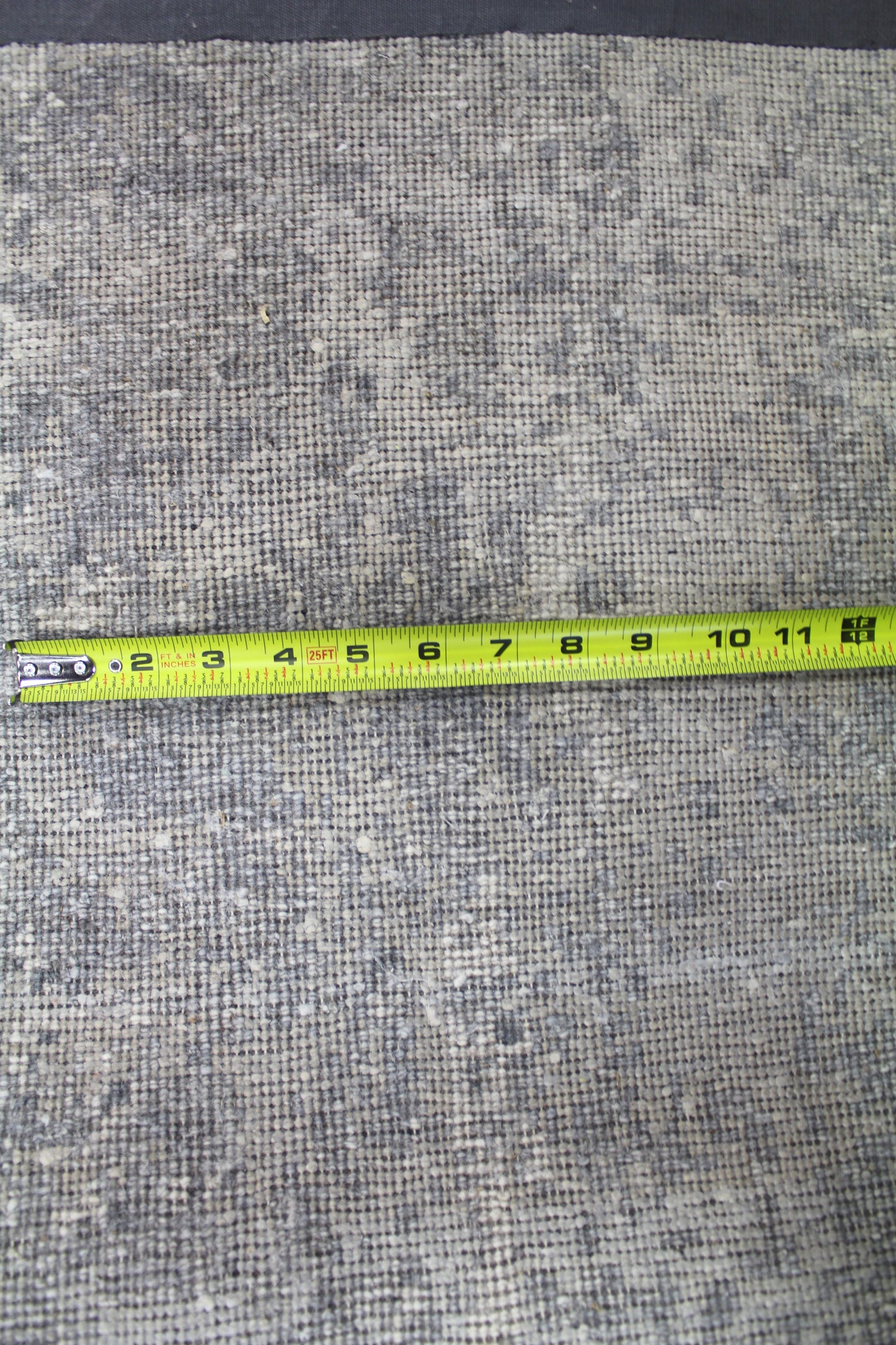 Close-up of handwoven rug texture, measured with tape measure showing detail.