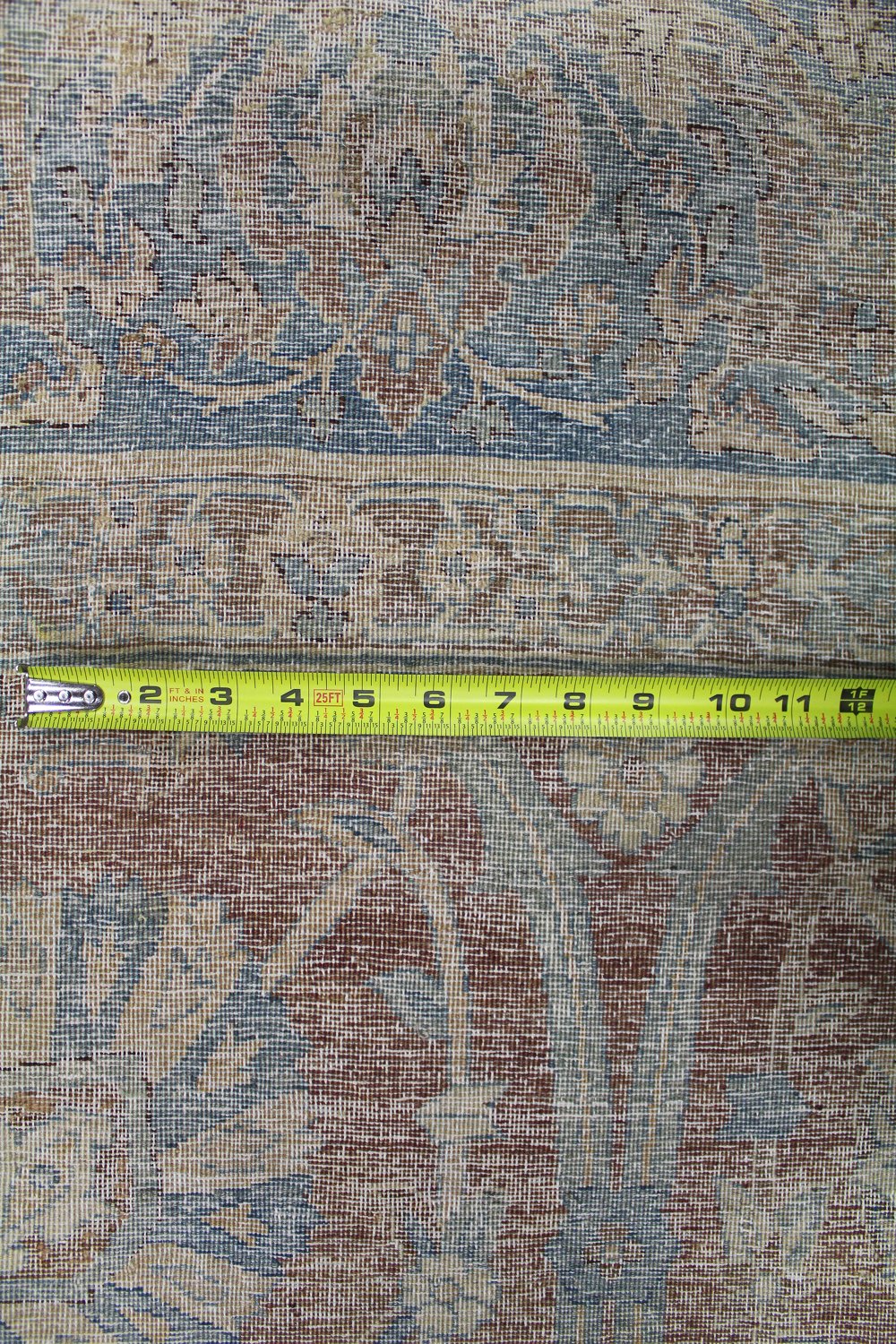 Close-up of antique rug's detailed handwoven pattern, measured with tape for accurate sizing.
