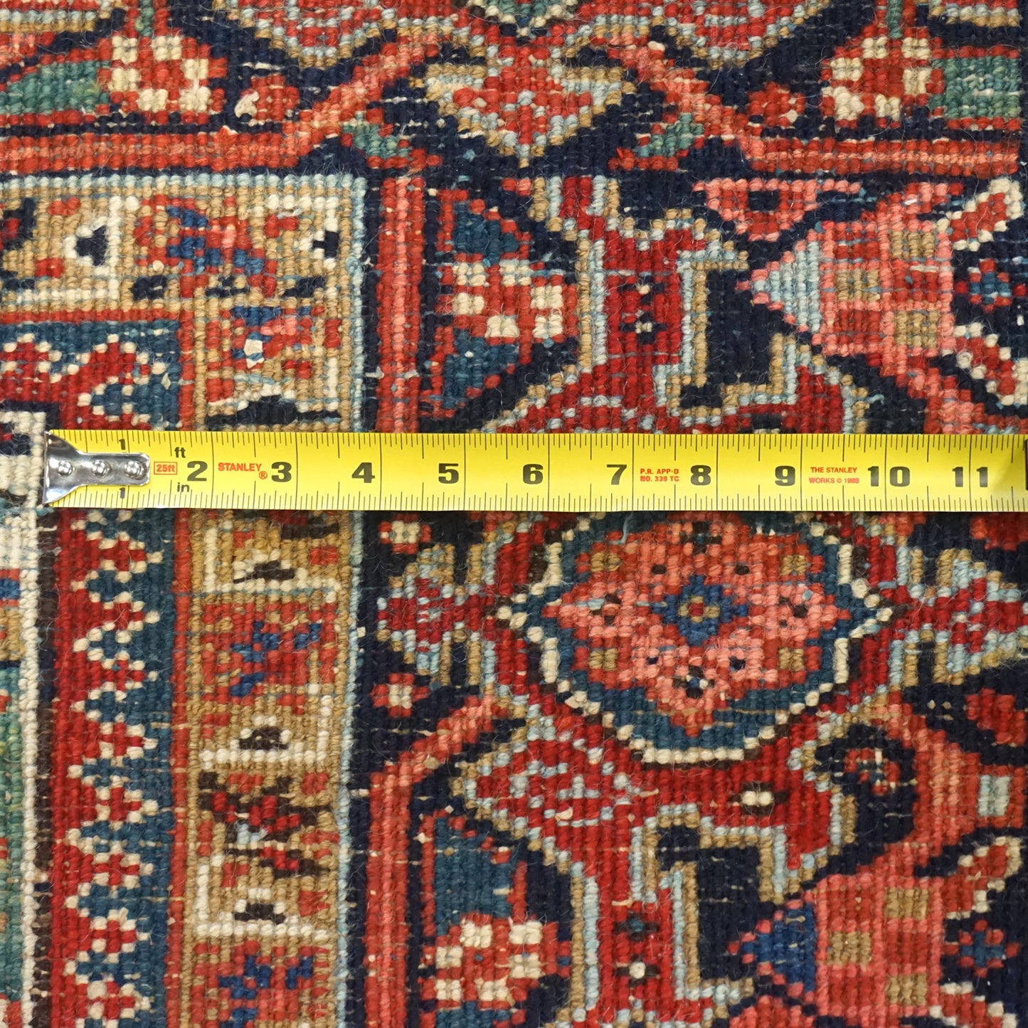 Close-up of antique Heriz rug detail, showcasing intricate handwoven pattern in red, blue, and beige tones.