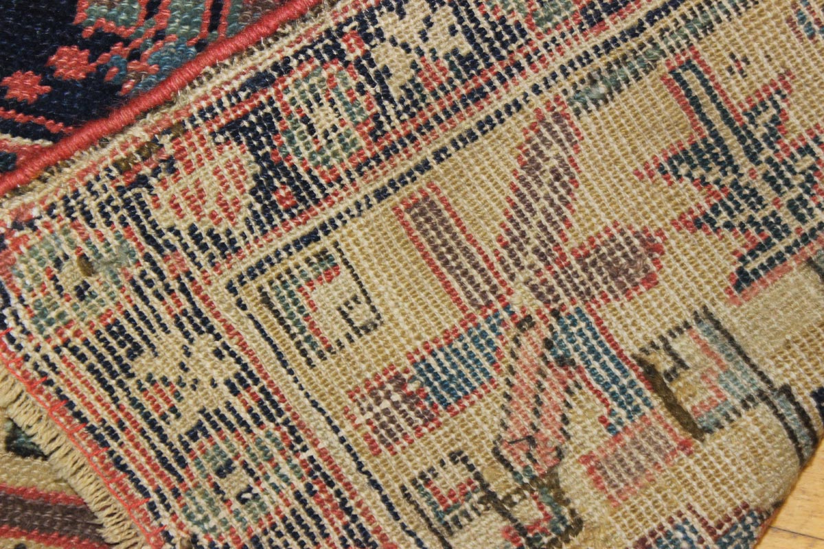 Close-up detail of antique rug's handwoven texture, showing multicolored geometric patterns in beige, red, and blue.