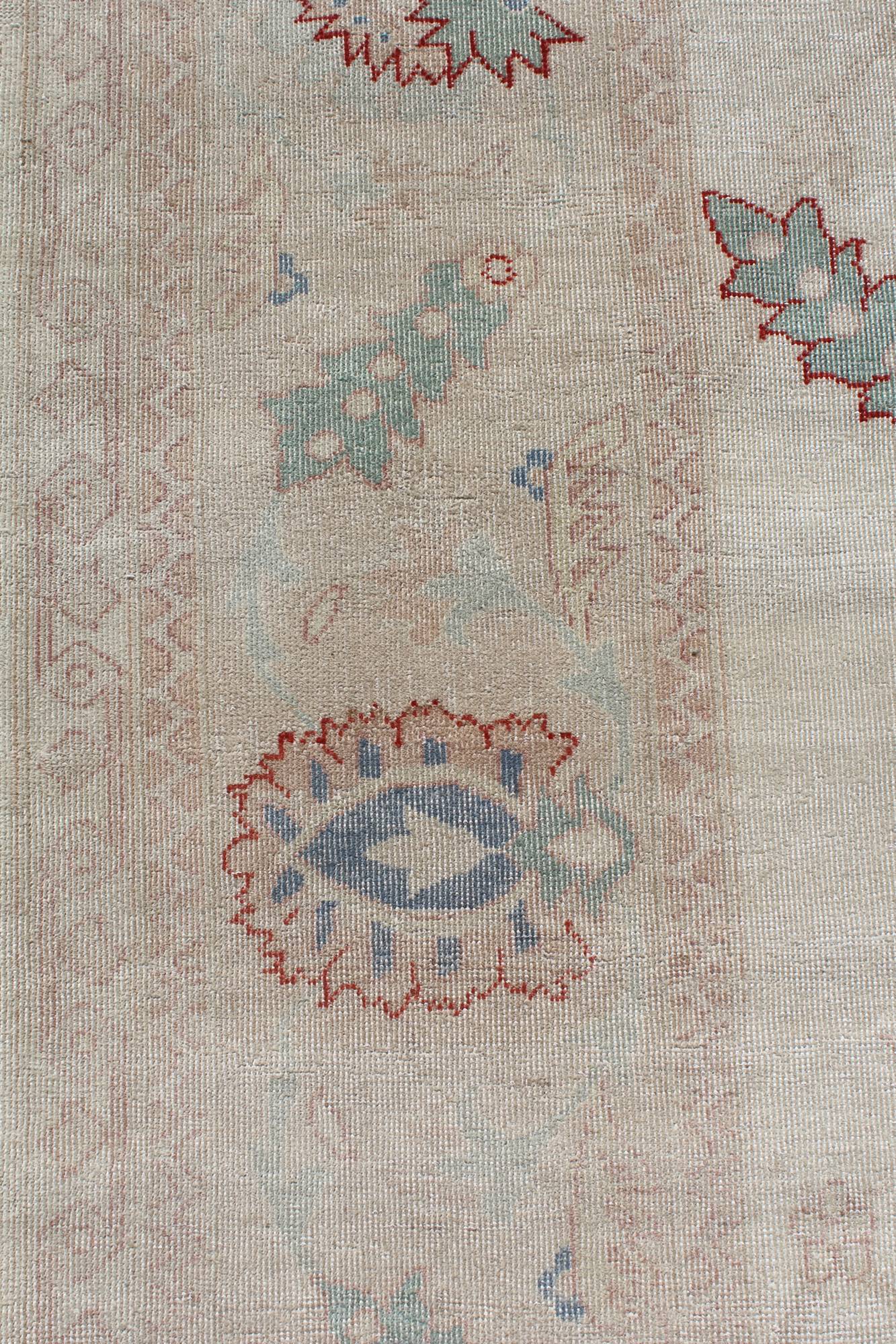 Handwoven rug detail: Beige background with muted blue, green, and red floral pattern.