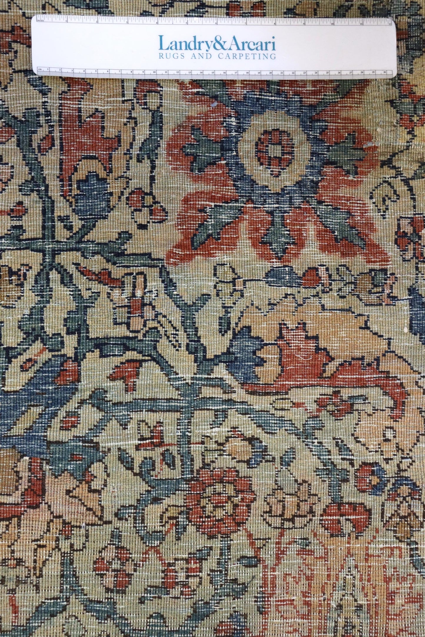 Close-up detail of antique Ferahan Sarouk rug, showcasing intricate floral pattern in muted reds, blues, and greens on a beige background.