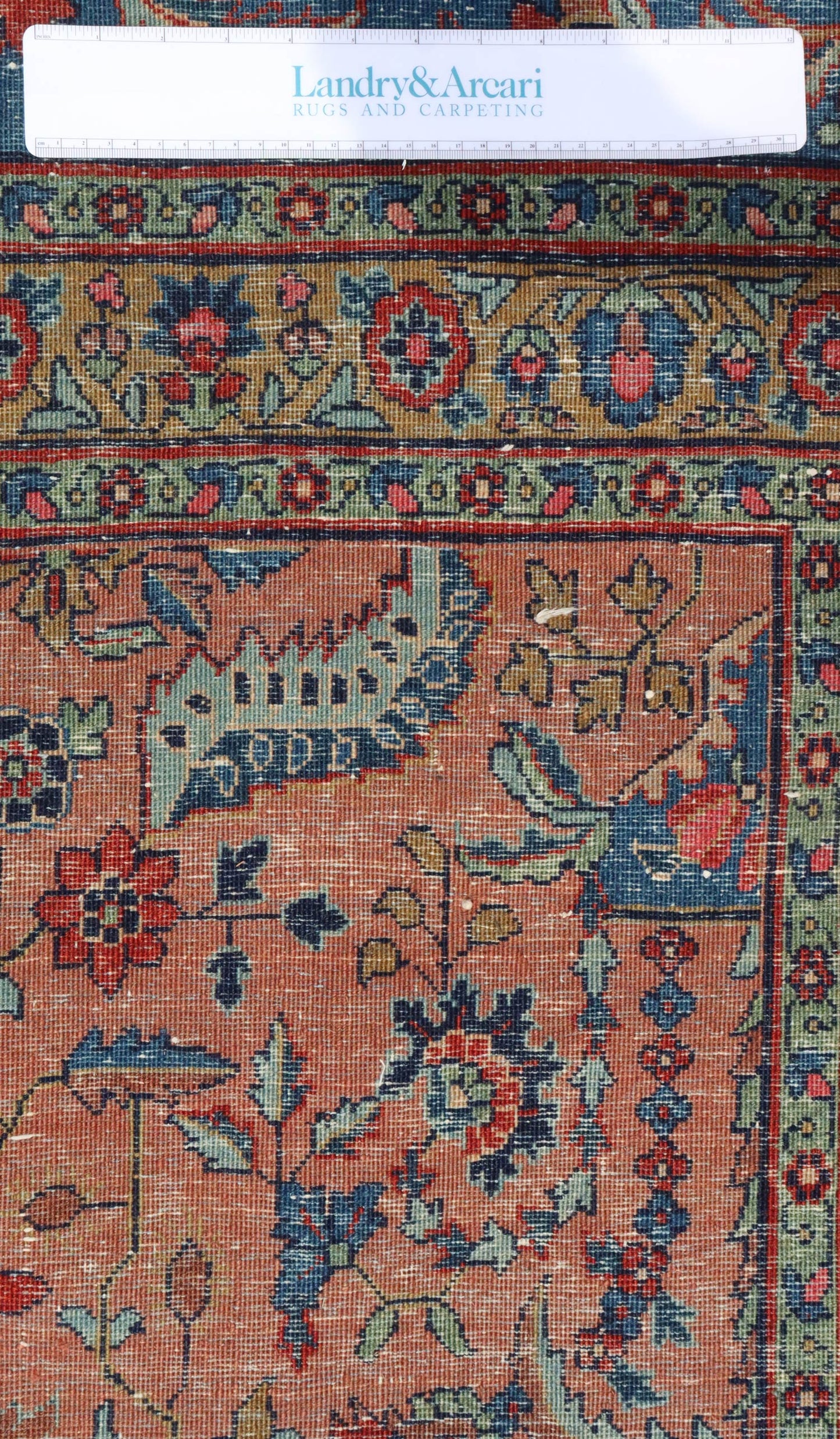 Detailed close-up of antique rug's handwoven floral pattern in red, blue, and green tones.
