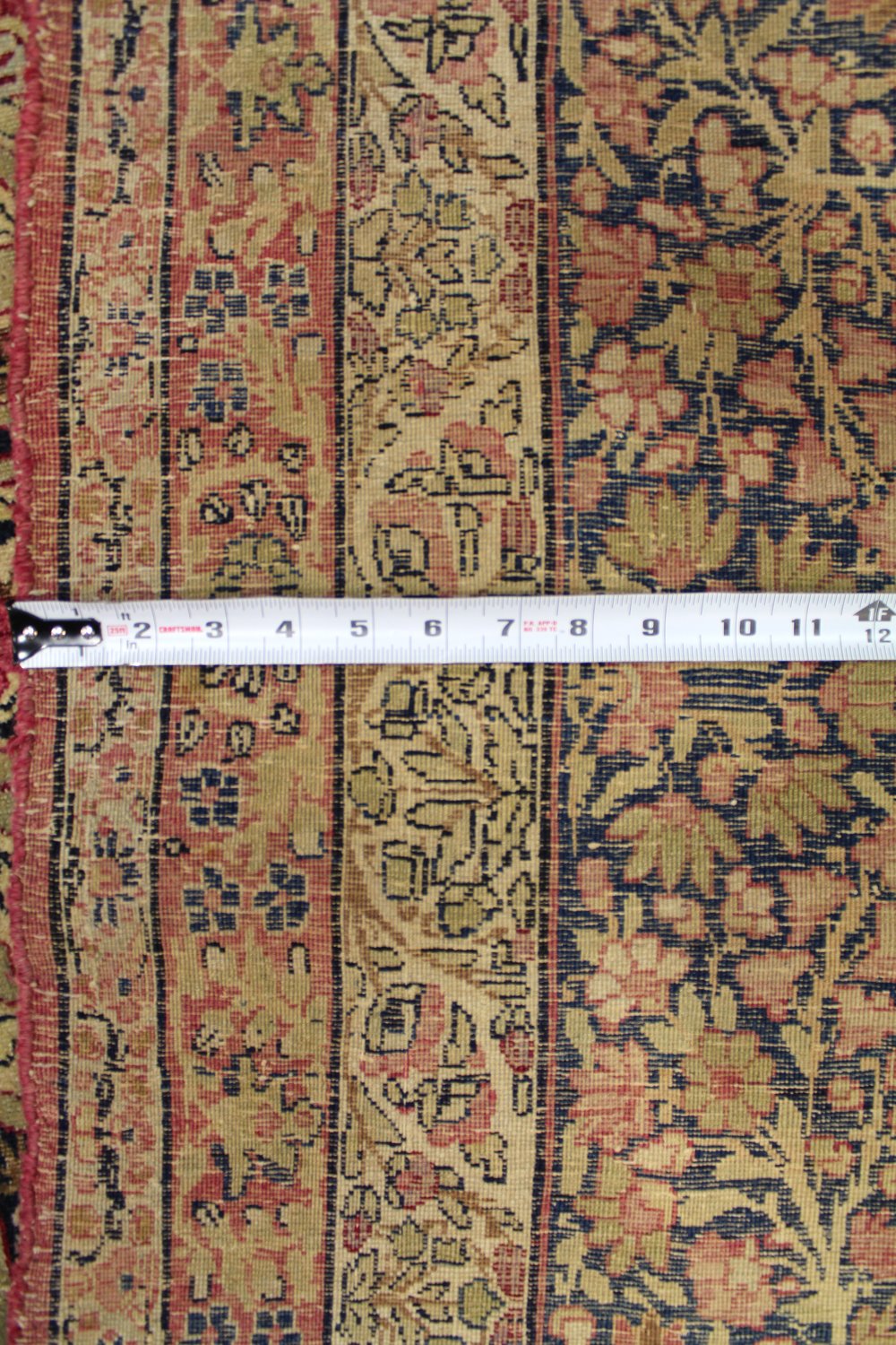 Close-up detail of antique Kerman rug, showcasing its intricate floral pattern in muted reds, beige, and navy.