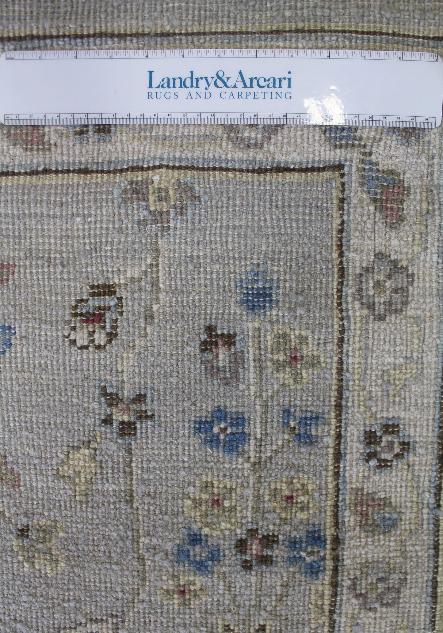Close-up of handwoven rug detail, showing pale neutral tones and subtle floral pattern.