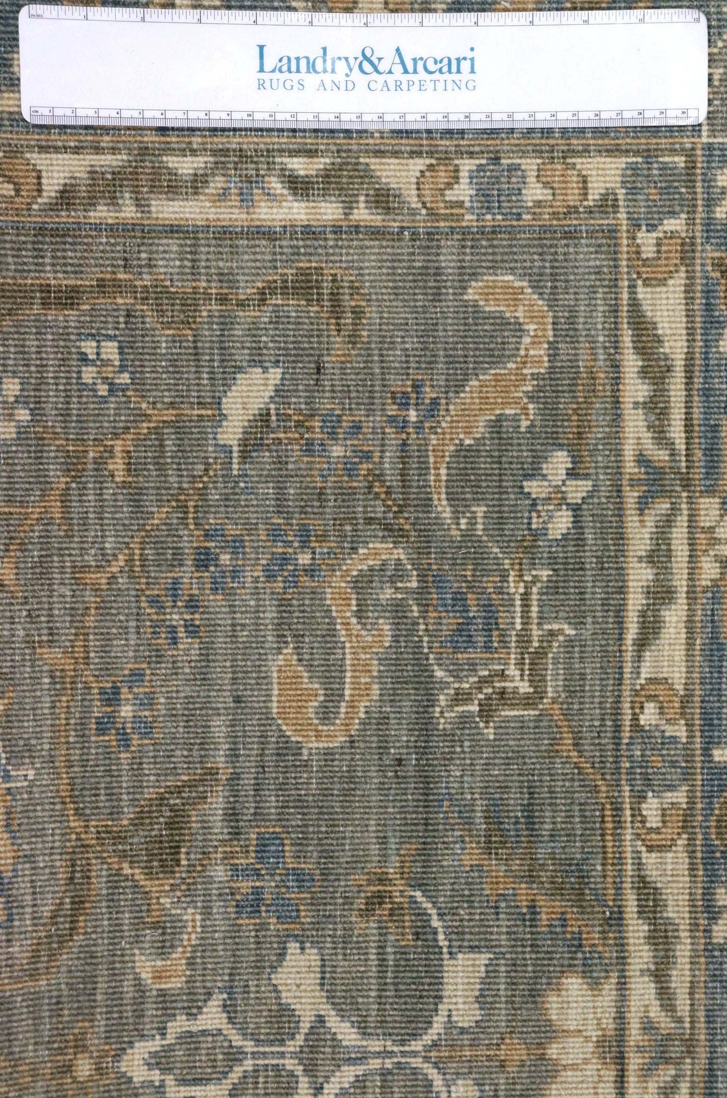 Close-up detail of a handwoven rug in muted blues and tans, showcasing intricate floral pattern.
