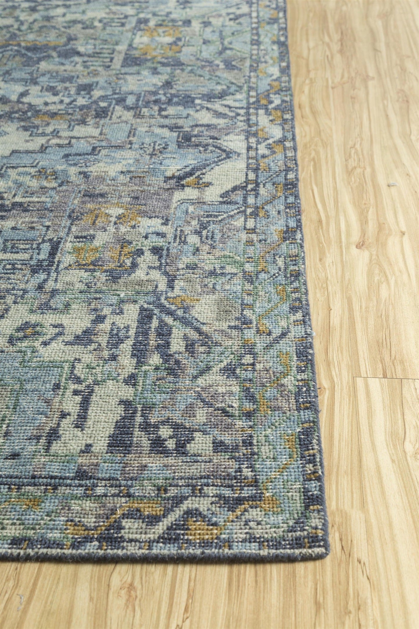 Handwoven rug detail, blue and gold pattern on light wood floor.