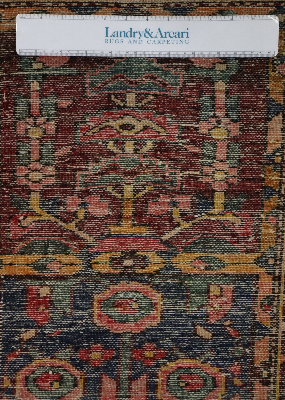 Close-up detail of an antique handwoven rug, showcasing intricate tribal patterns in rich reds, blues, and golds.