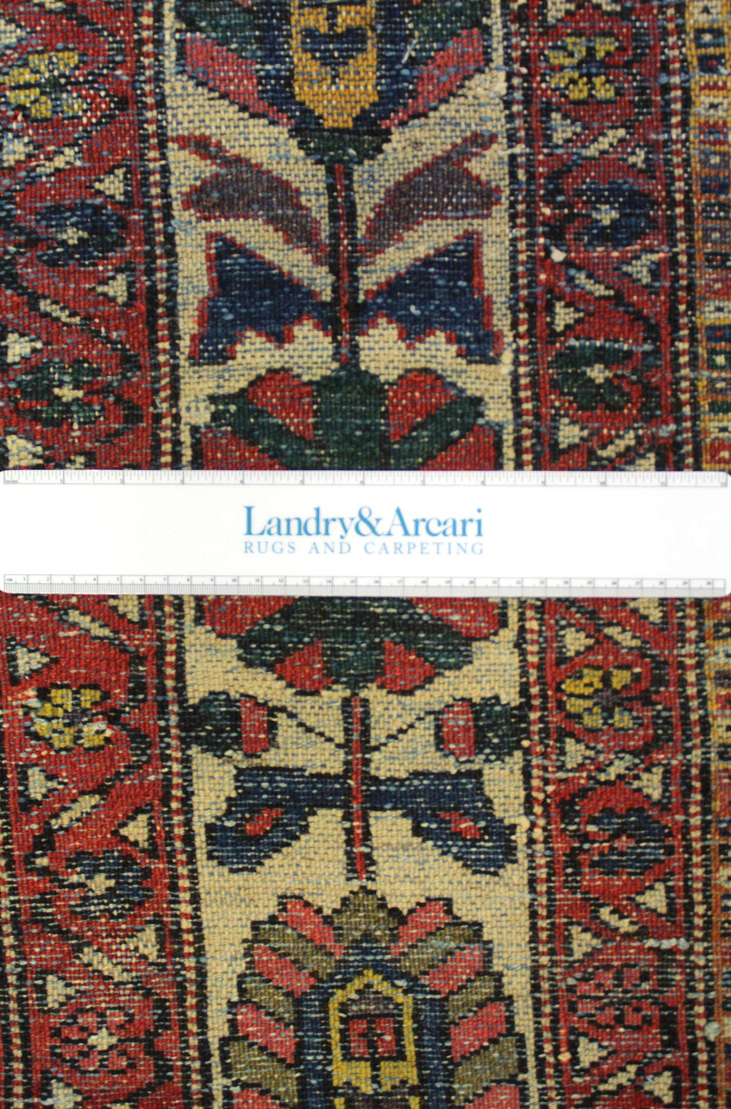 Close-up detail of antique tribal rug's handwoven floral pattern, showcasing rich reds and blues.