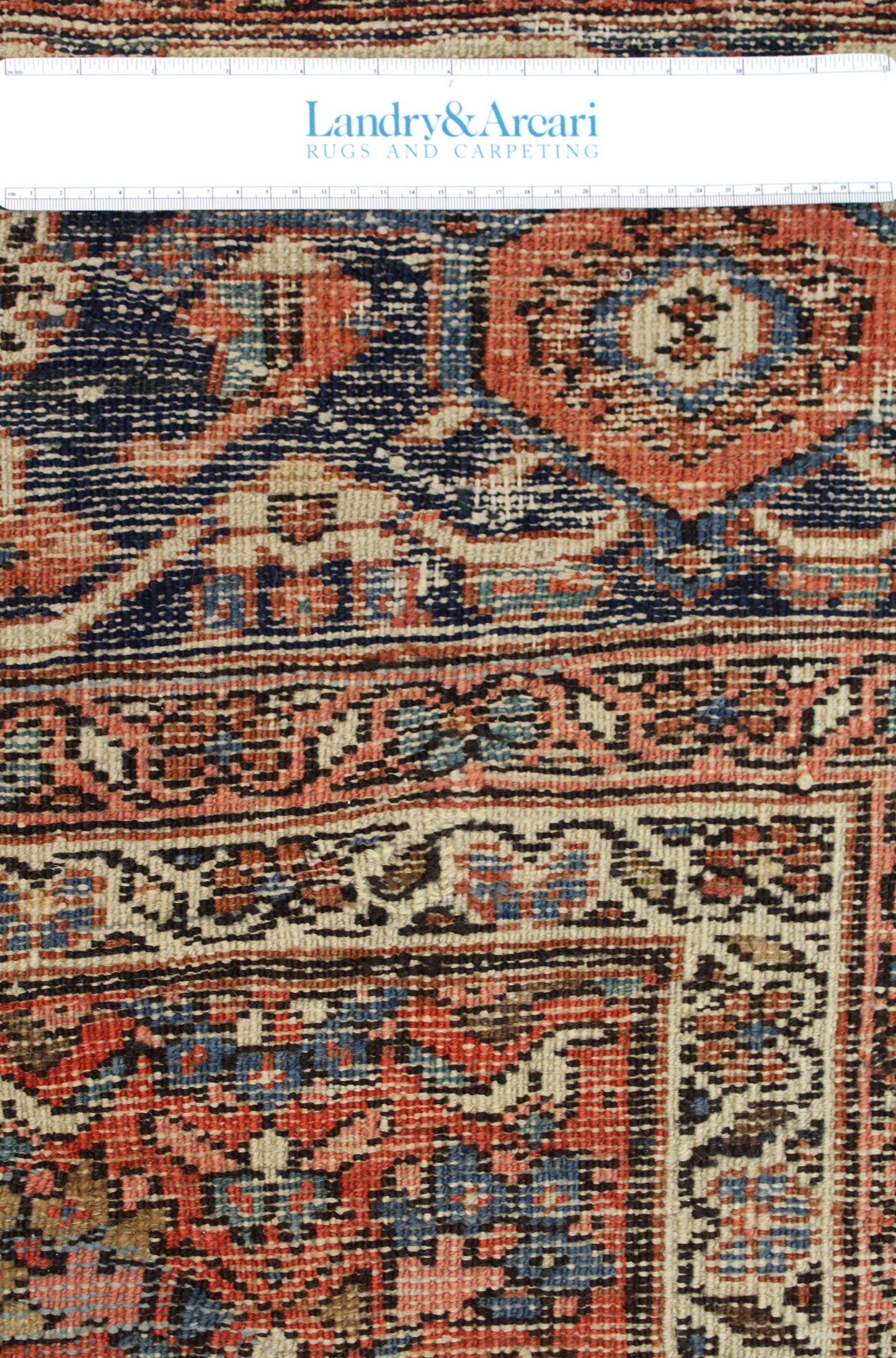 Close-up detail of antique handwoven rug, showcasing intricate red, blue, and beige patterns.