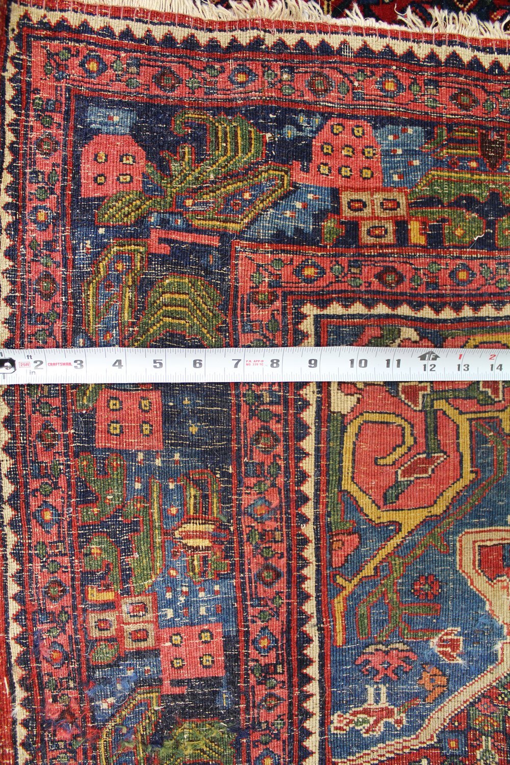 Handwoven tribal rug detail, showcasing vibrant reds, blues, and greens in a detailed pattern, measured with a tape measure.