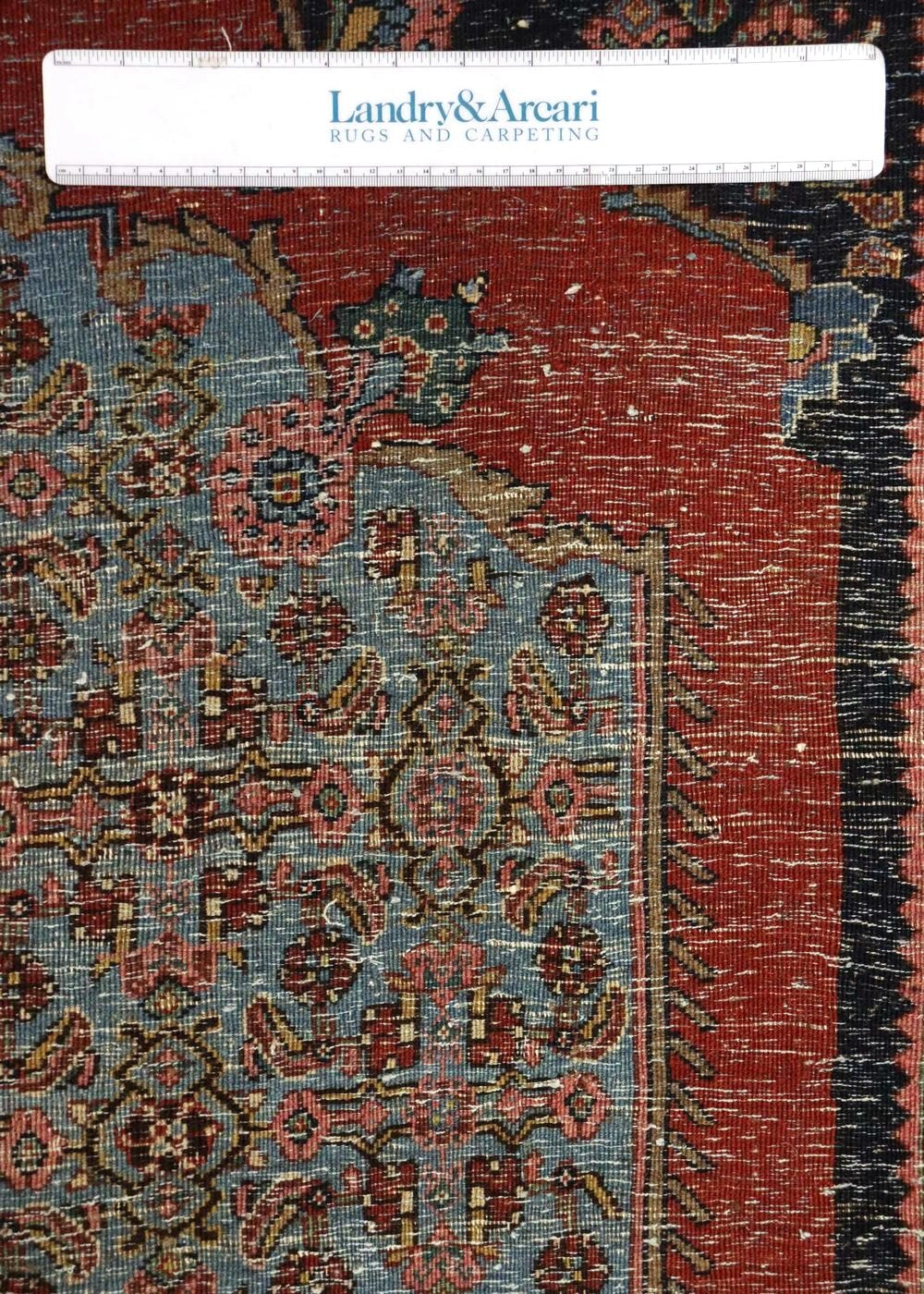 Detailed close-up of antique tribal rug's handwoven texture, showcasing faded reds and blues.