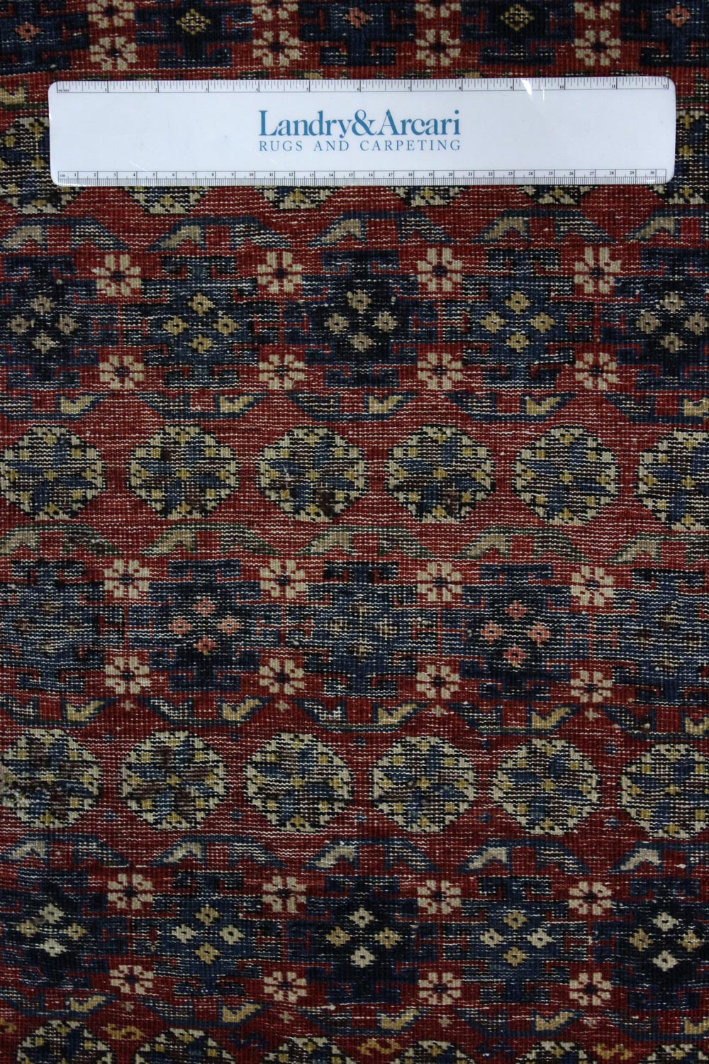 Close-up detail of an antique tribal rug with a red and navy blue repeating pattern.