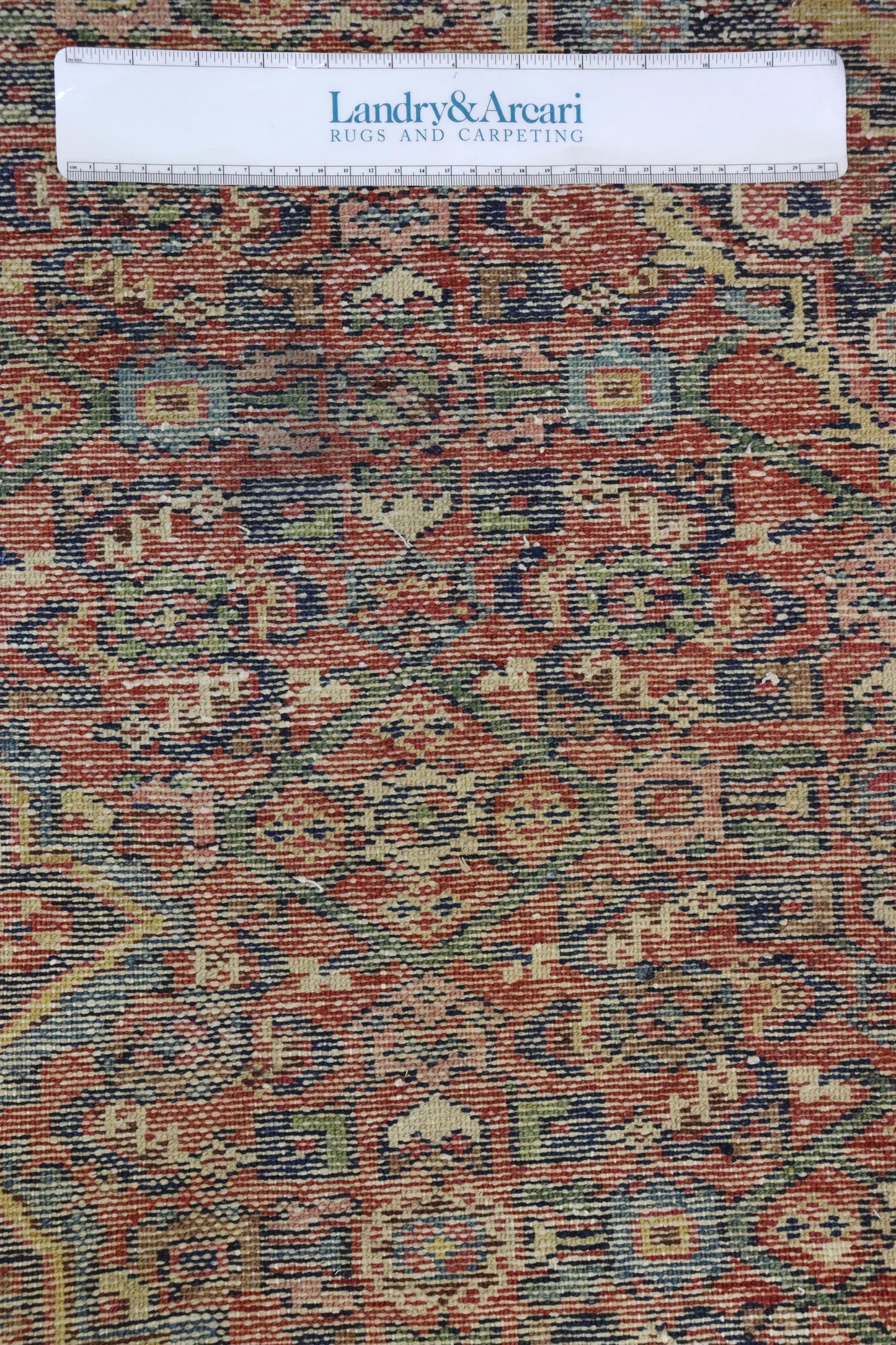 Close-up of antique Hamadan rug detail, showcasing intricate handwoven pattern in red, blue, and green tones.