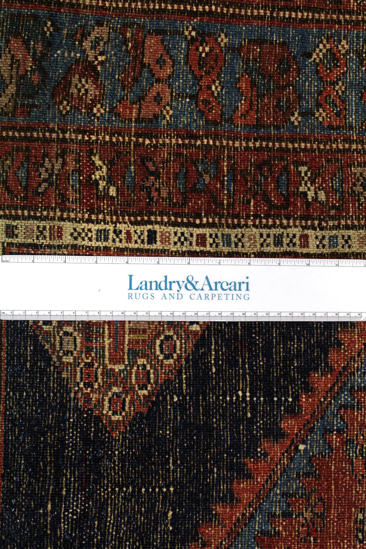 Close-up detail of antique Hamadan rug showing intricate, handwoven pattern in rich reds, blues, and blacks.