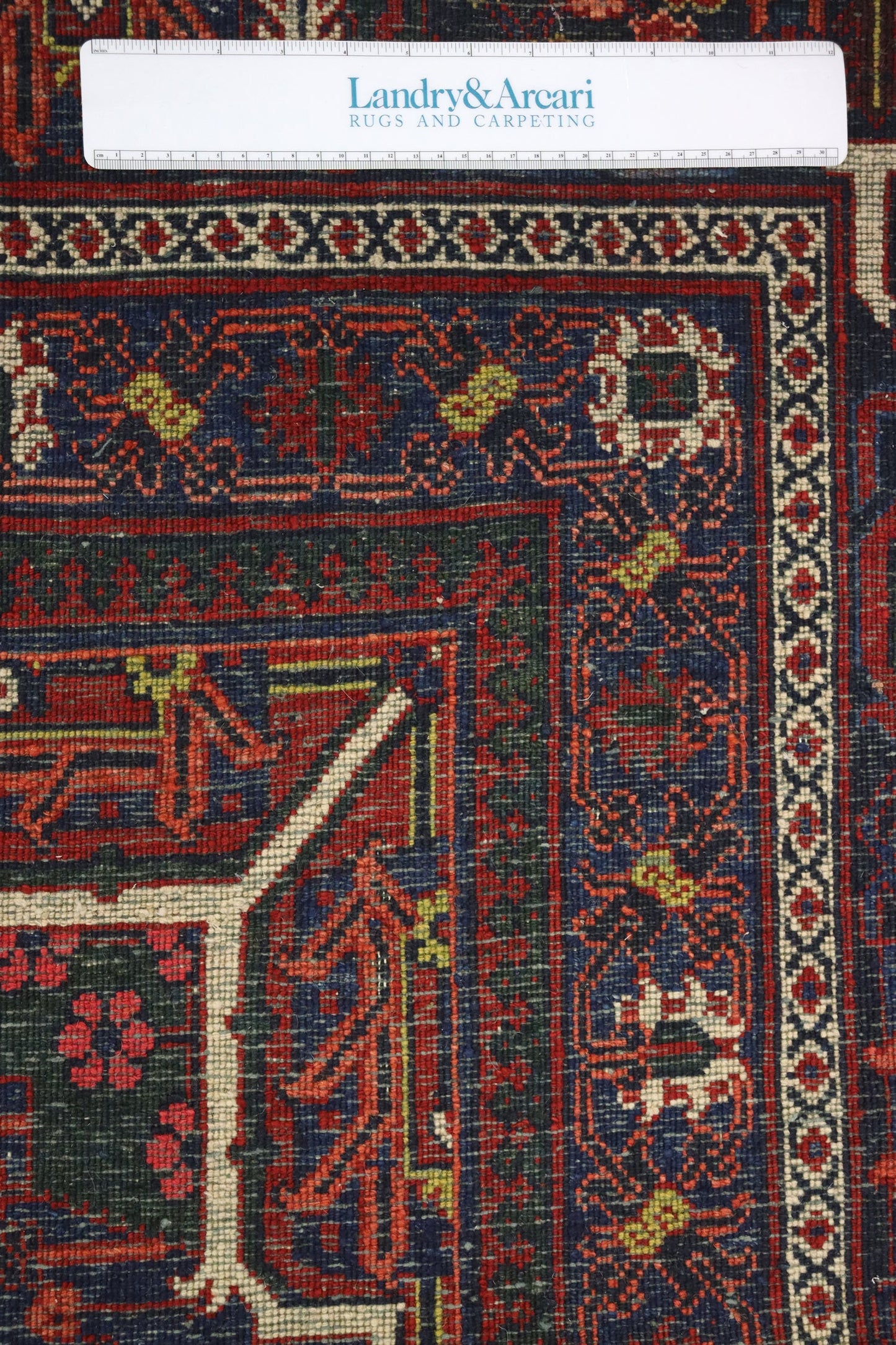 Close-up detail of an antique handwoven rug, showcasing intricate red, blue, and ivory patterns.