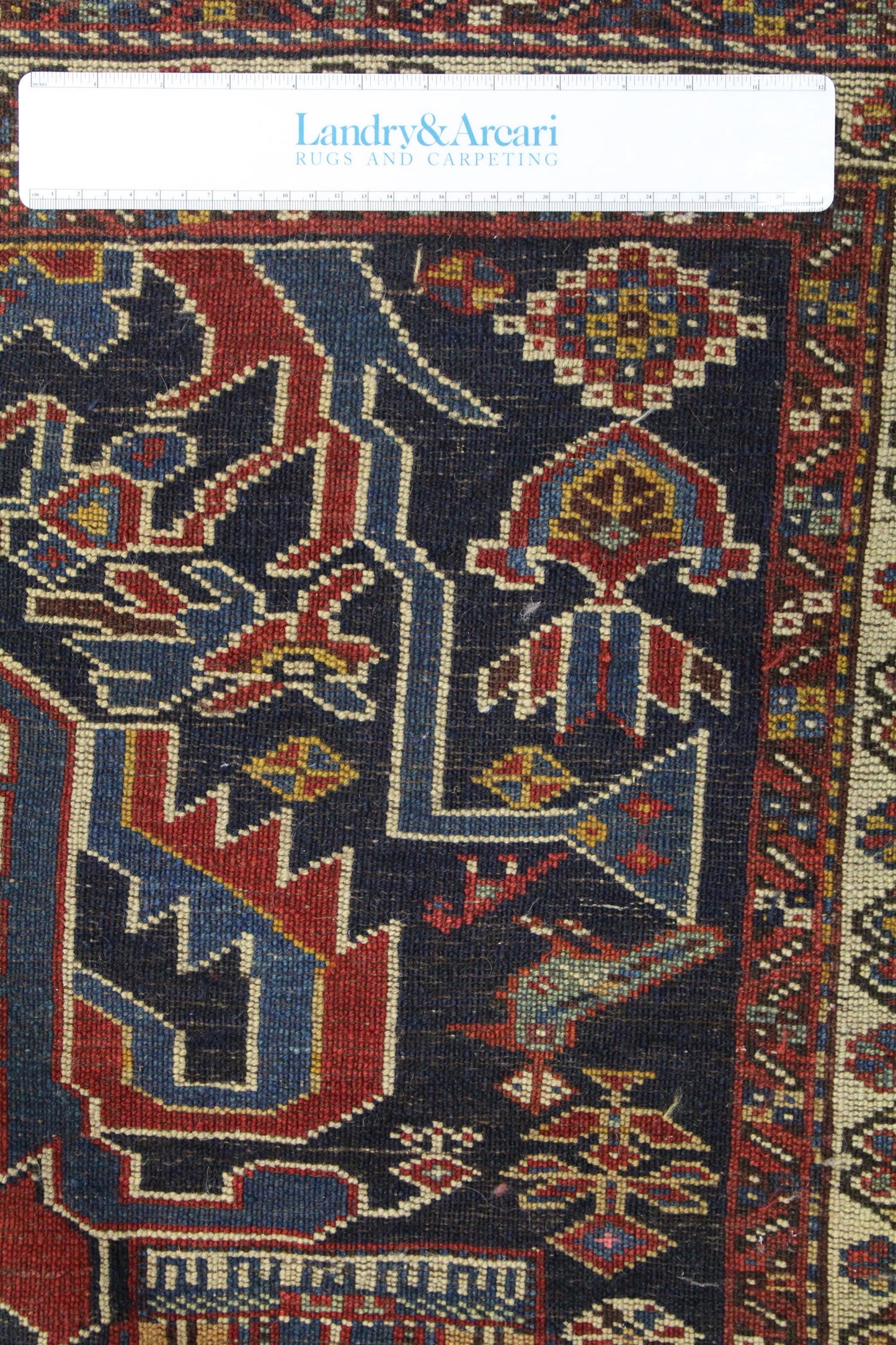 Close-up detail of antique tribal rug, showcasing handwoven pattern in deep blues, reds, and creams.