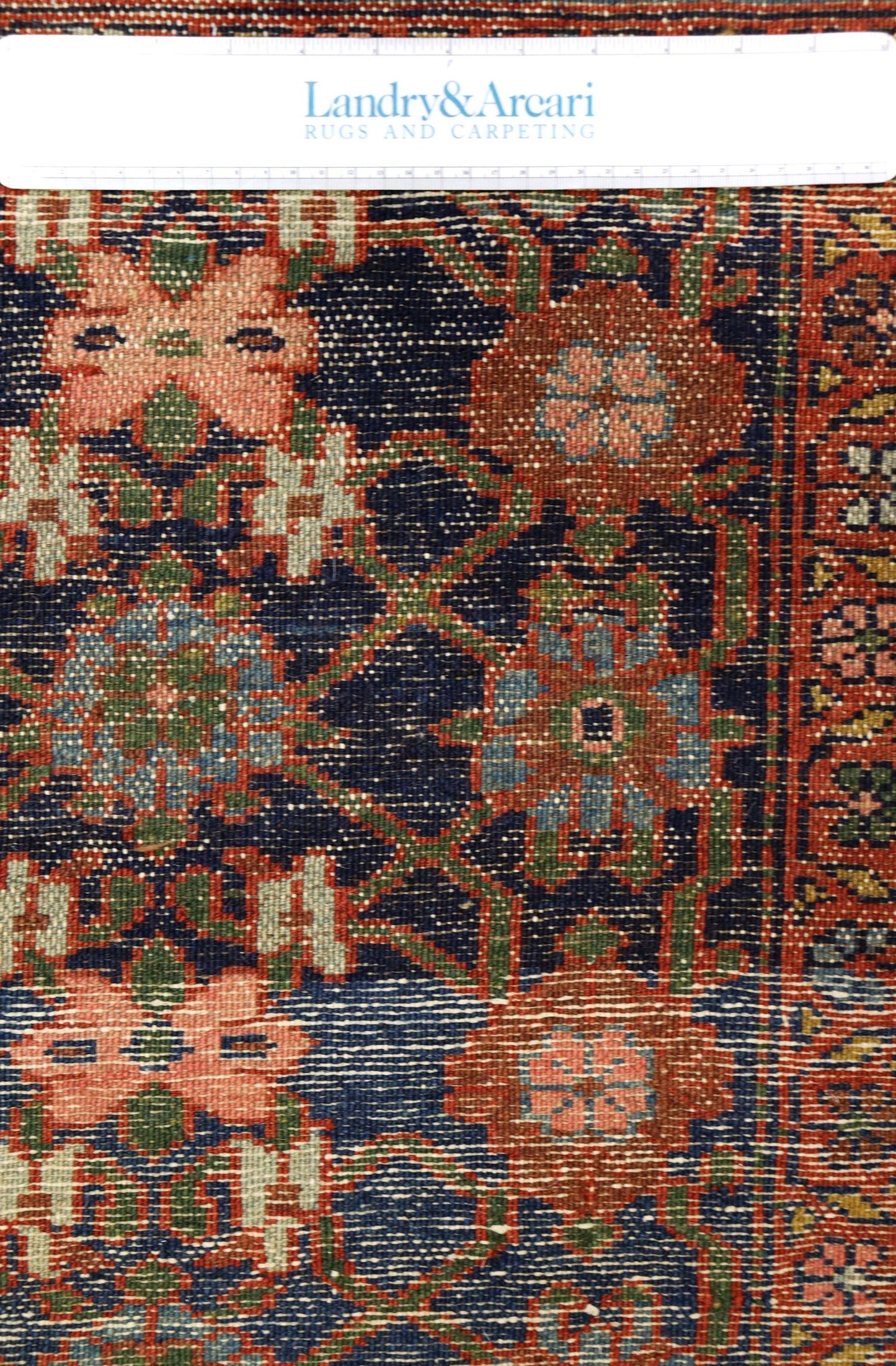 Intricate detail of an antique handwoven tribal rug, showcasing a rich palette of reds, blues, and greens in a floral pattern.