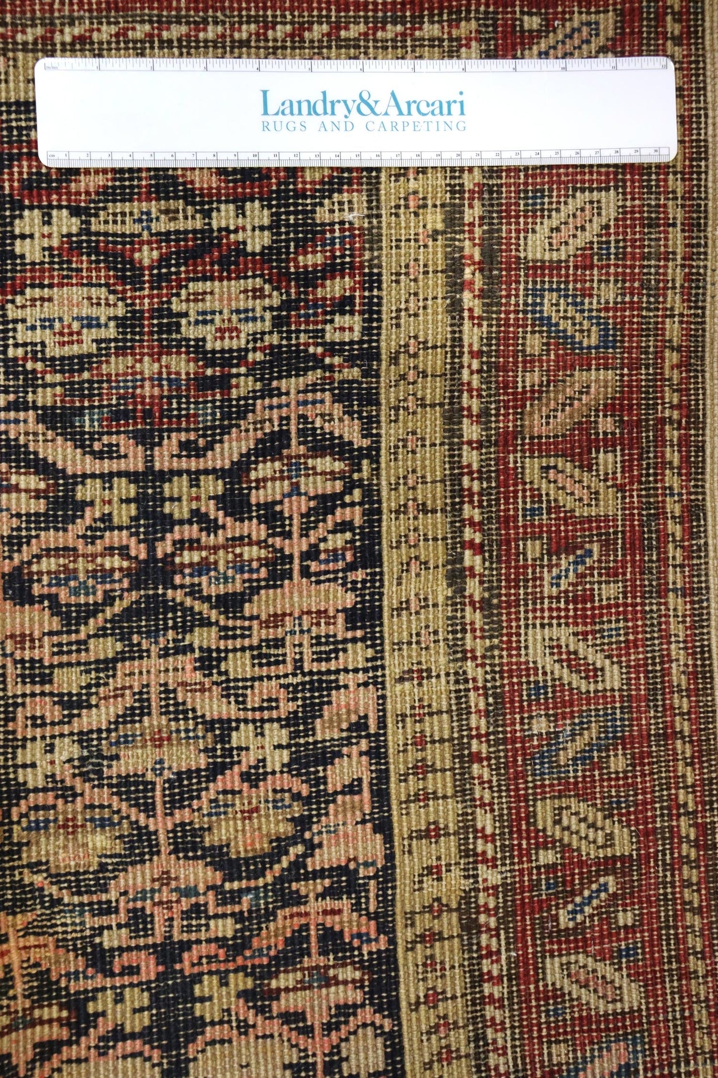 Close-up detail of antique Persian rug, showcasing handwoven design in red, beige, and navy.