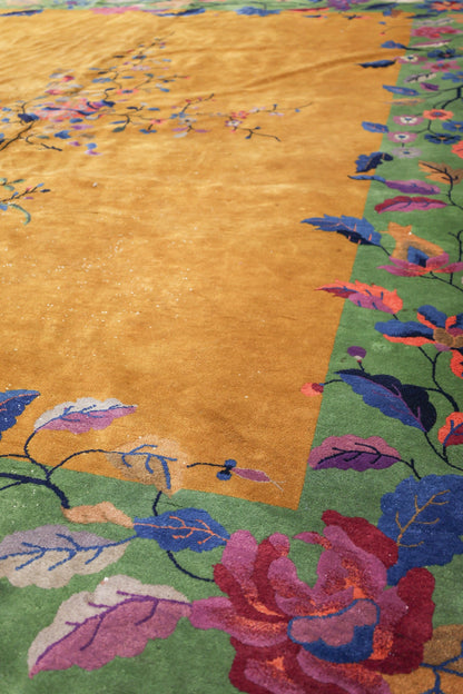 Handwoven Art Deco rug detail: mustard yellow field with a green floral border, showcasing colorful blossoms and leaves.
