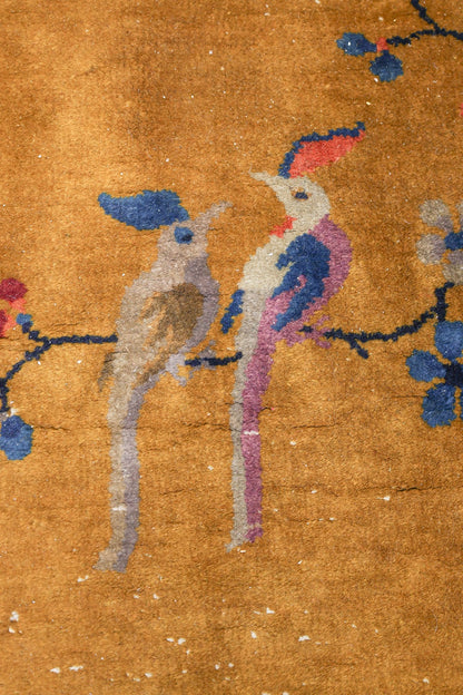 Detail of an antique rug featuring handwoven birds on a gold background.
