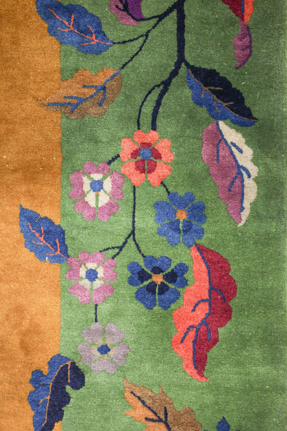 Detail of an antique rug with a handwoven floral and leaf design in shades of green, blue, orange, and red.
