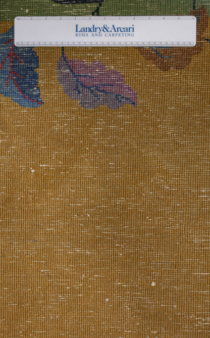 Close-up detail of an antique Art Deco rug's textured weave, showcasing a gold base with multicolored leaf pattern.
