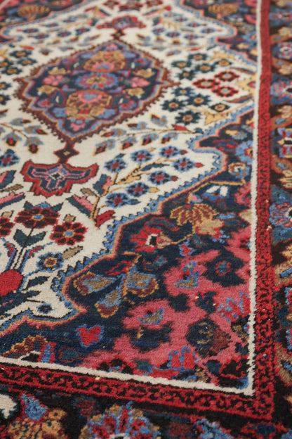 Close-up of antique rug's intricate floral pattern in deep reds, blues, and creams.
