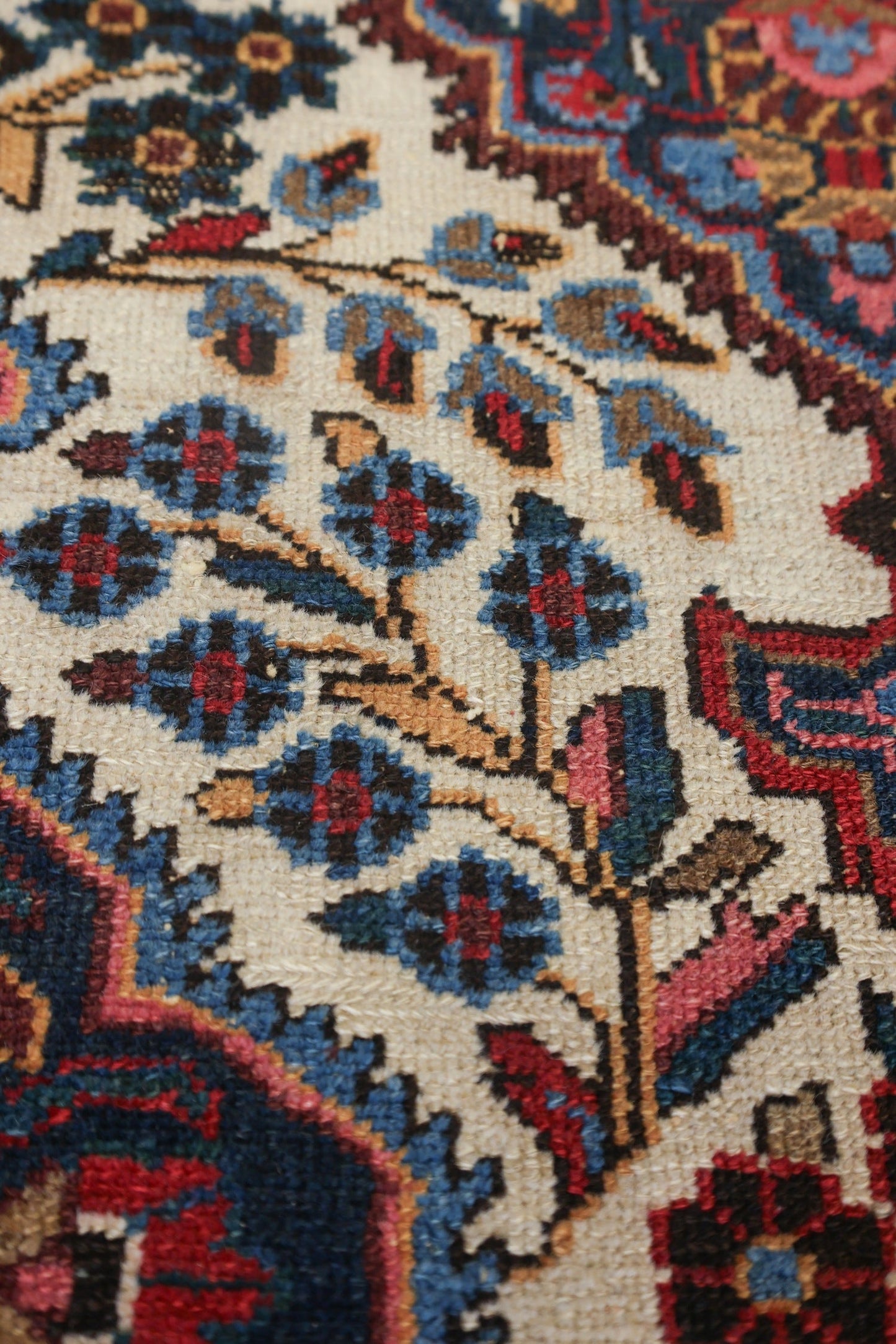 Close-up of antique rug detail, showcasing handwoven floral pattern in blue, red, and beige.
