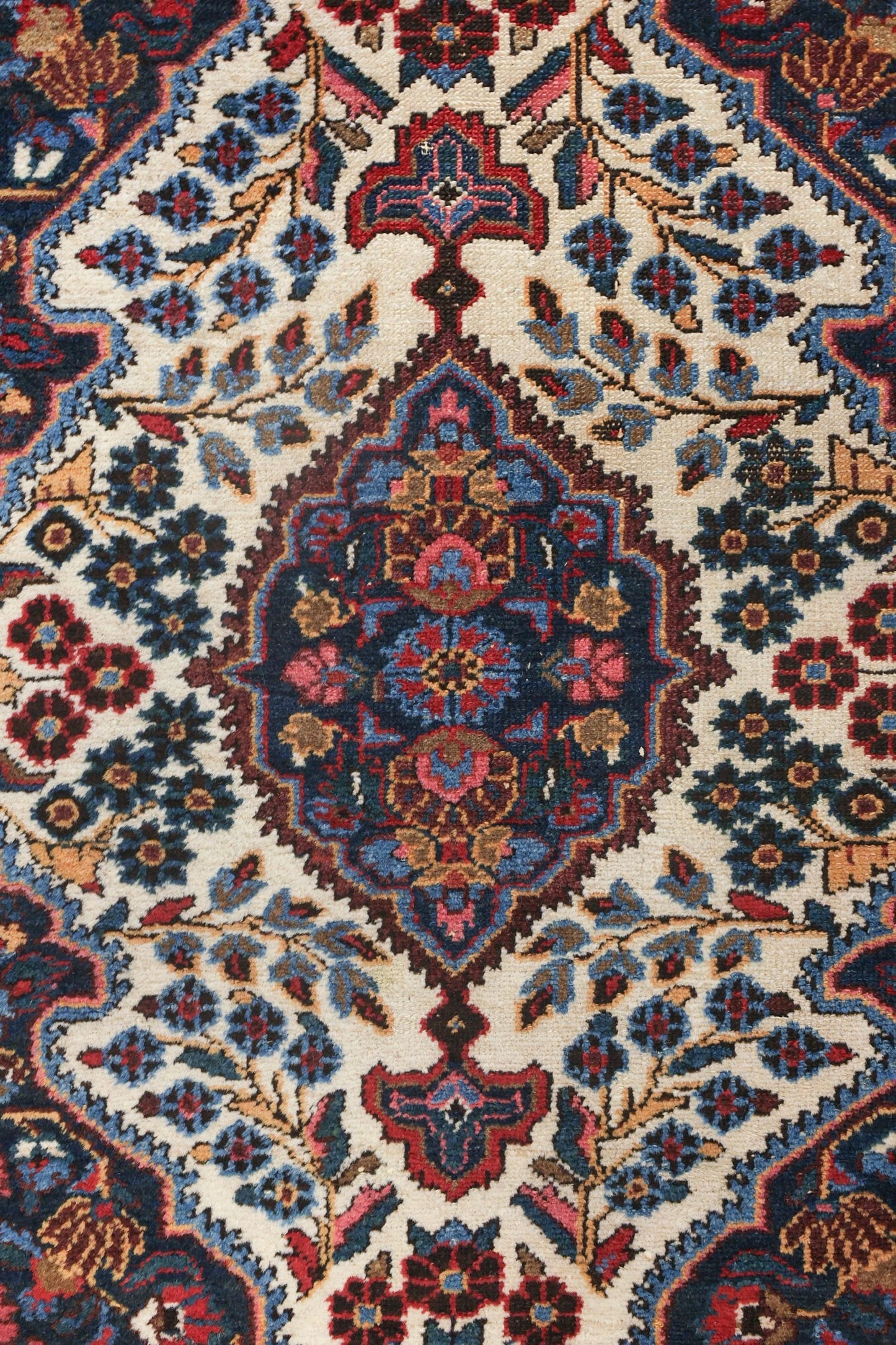 Handwoven rug detail: intricate floral pattern in navy, red, and beige on an off-white background.
