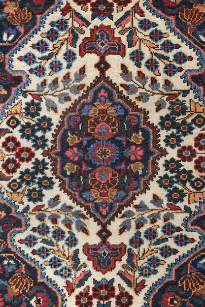 Handwoven rug detail: intricate floral pattern in navy, red, and beige on an off-white background.
