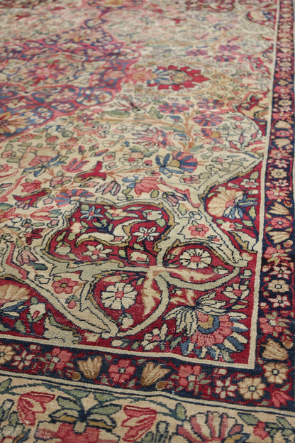 Detail of antique Kerman rug, showcasing intricate floral pattern in red, beige, and navy.
