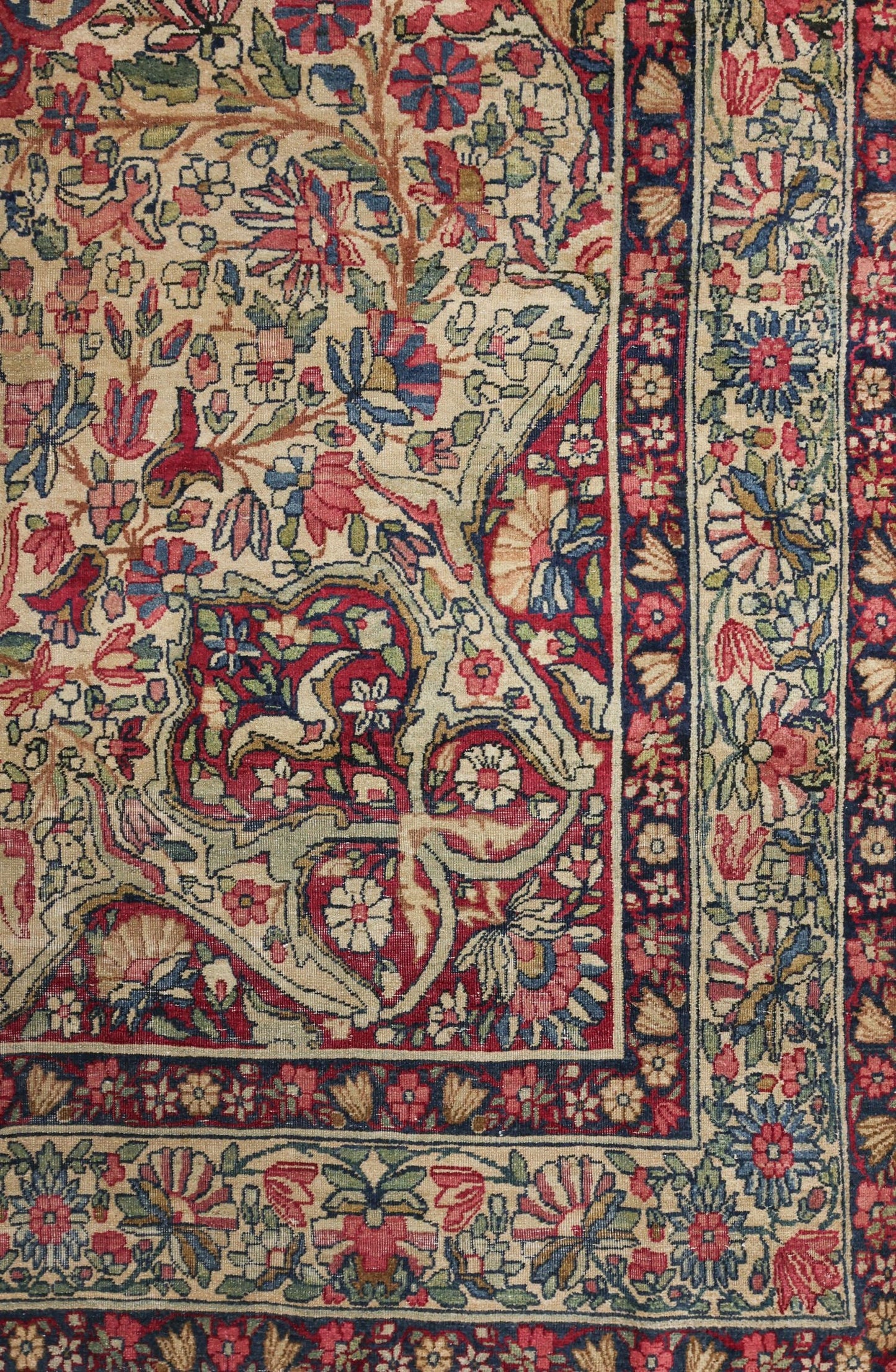 Detail of antique Kerman rug, showcasing intricate floral pattern in red, beige, and blue.
