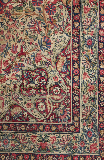 Detail of antique Kerman rug, showcasing intricate floral pattern in red, beige, and blue.
