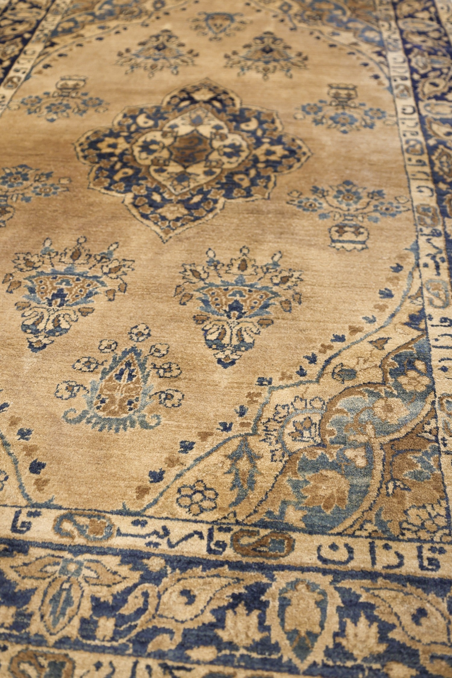 Close-up of a beige handwoven rug with intricate blue and brown floral patterns.
