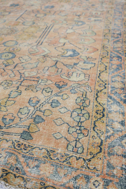Close-up of a peach-toned antique rug with a detailed, handwoven floral pattern in muted blues and greens.
