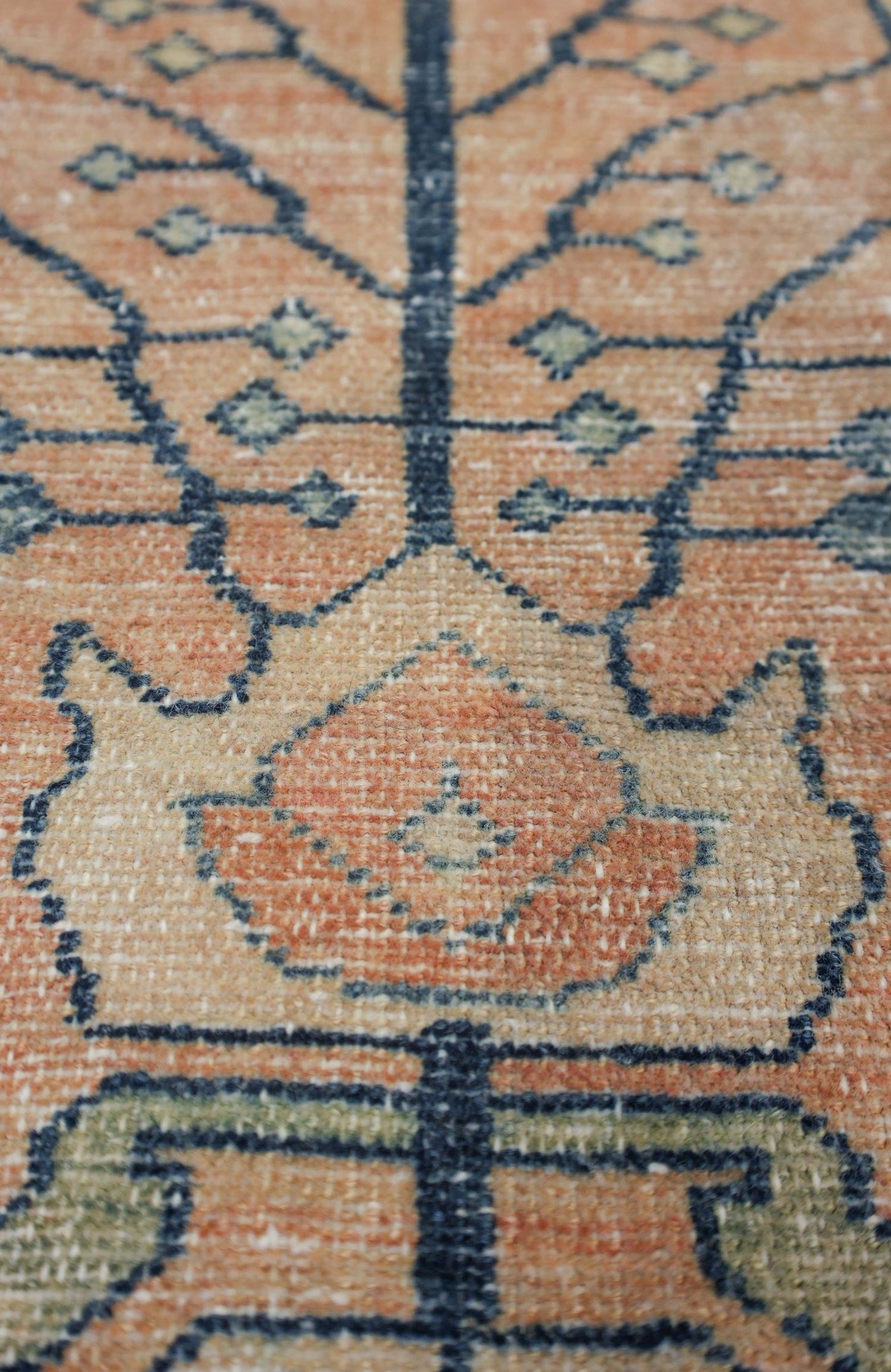 Close-up of antique rug's handwoven detail; muted orange, beige, and blue pattern.

