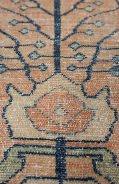 Close-up of antique rug's handwoven detail; muted orange, beige, and blue pattern.
