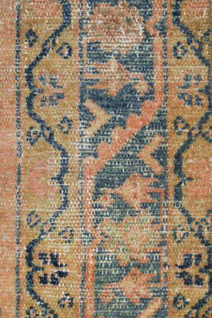 Close-up of antique rug's handwoven detail, featuring a muted peach and blue floral pattern.
